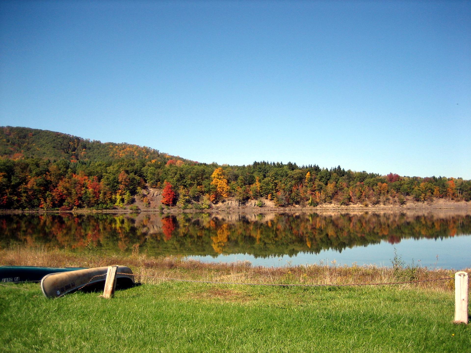 A calm lake reflects colorful autumn trees under a clear blue sky.
