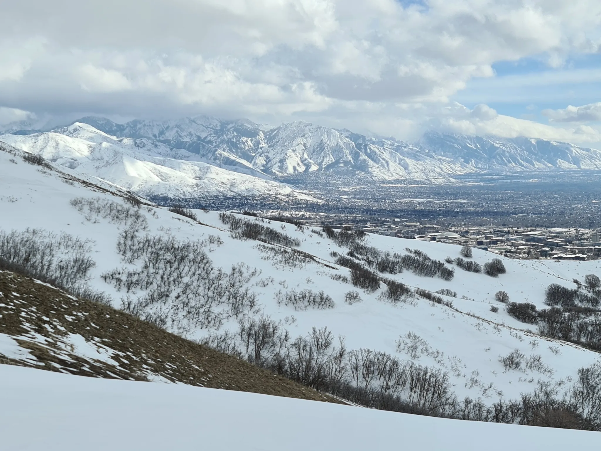 Expansive view of snow-covered mountains overlooking a distant city under cloudy skies. - Terror Ridge and Bobsled Loop