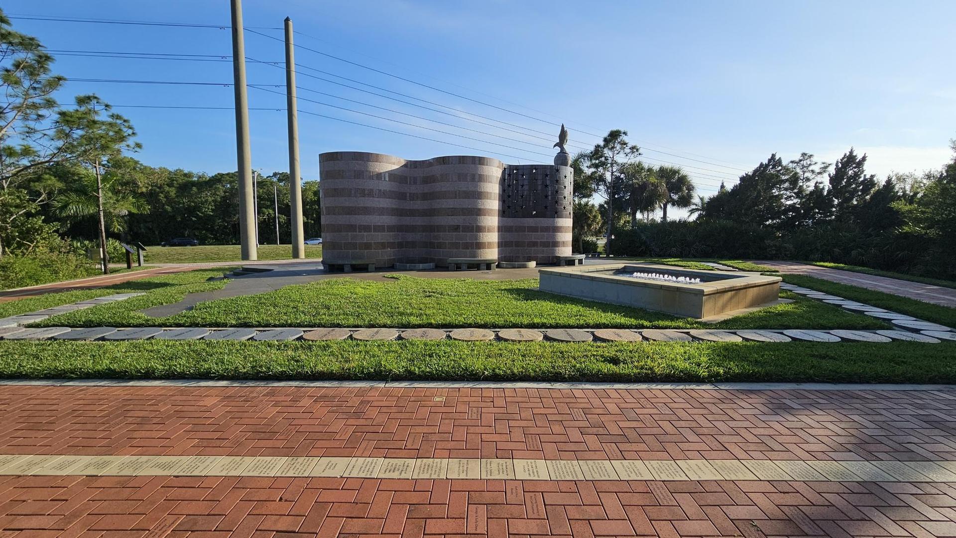Large concrete structures and a rectangular water feature on a sunny grassy area.