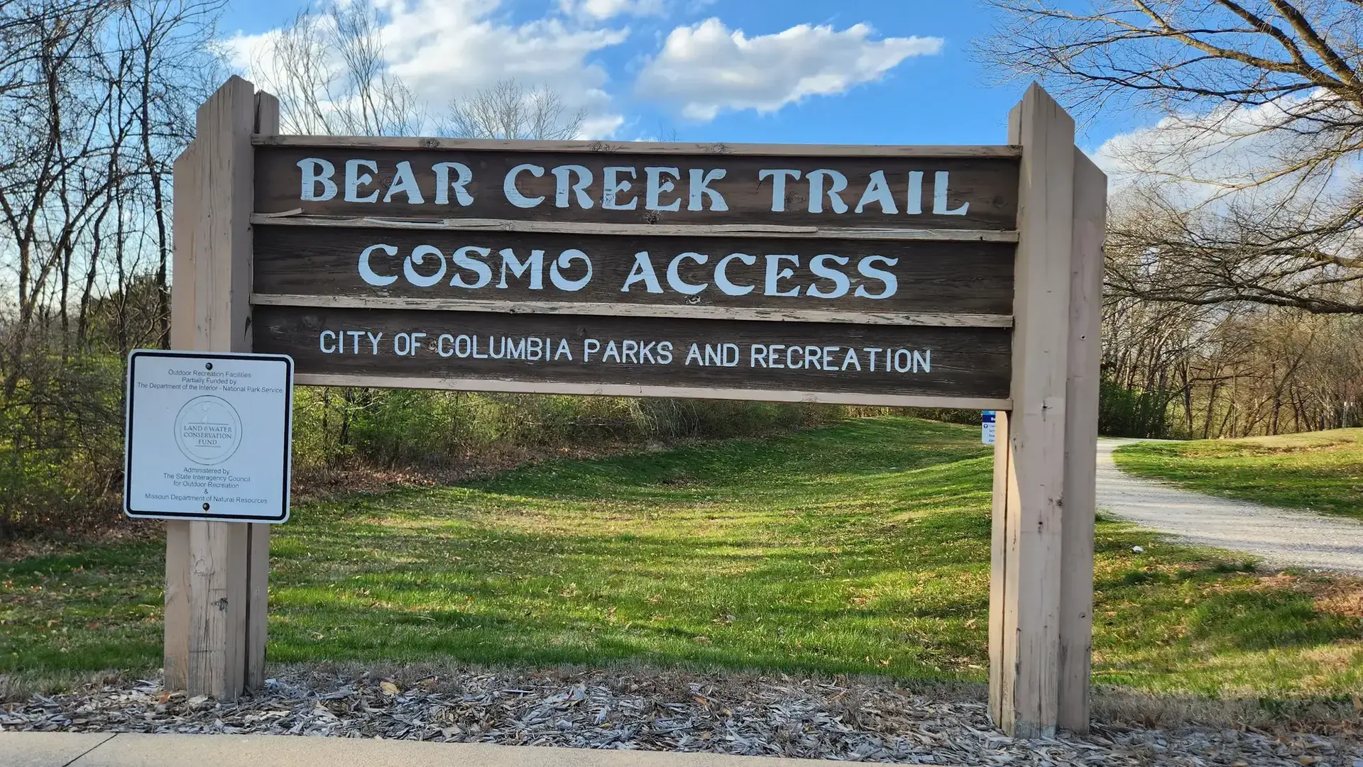 Large wooden sign at a trail entrance on a bright, cloudy day.