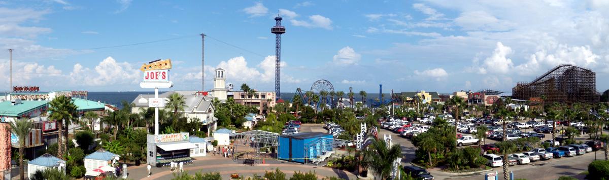 Panoramic view of a bustling amusement park with rides and a full parking lot.