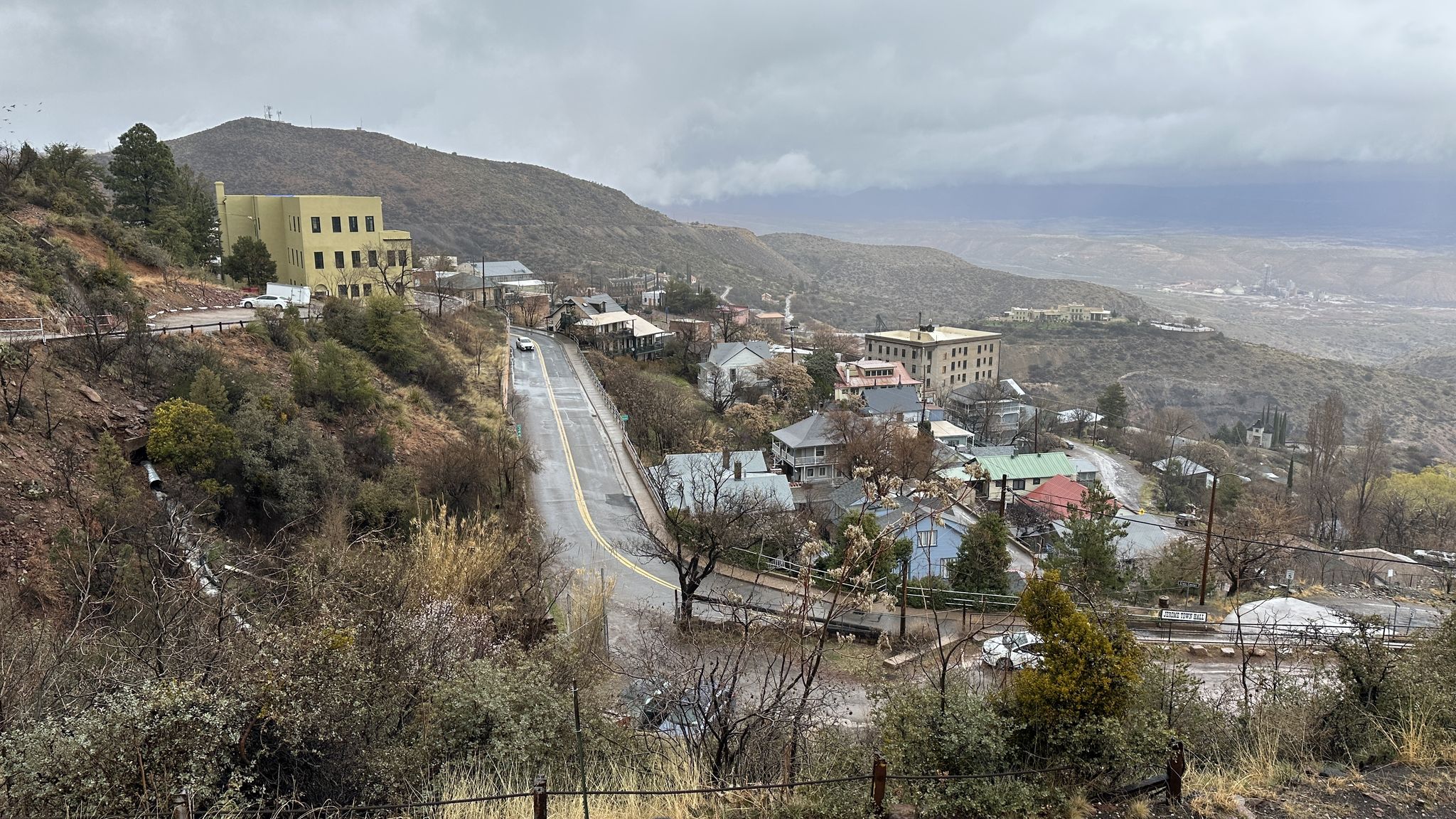 Overcast view of a hillside town with a winding road and distant mountains. - Jerome Mine Museum loop from Clarkdale