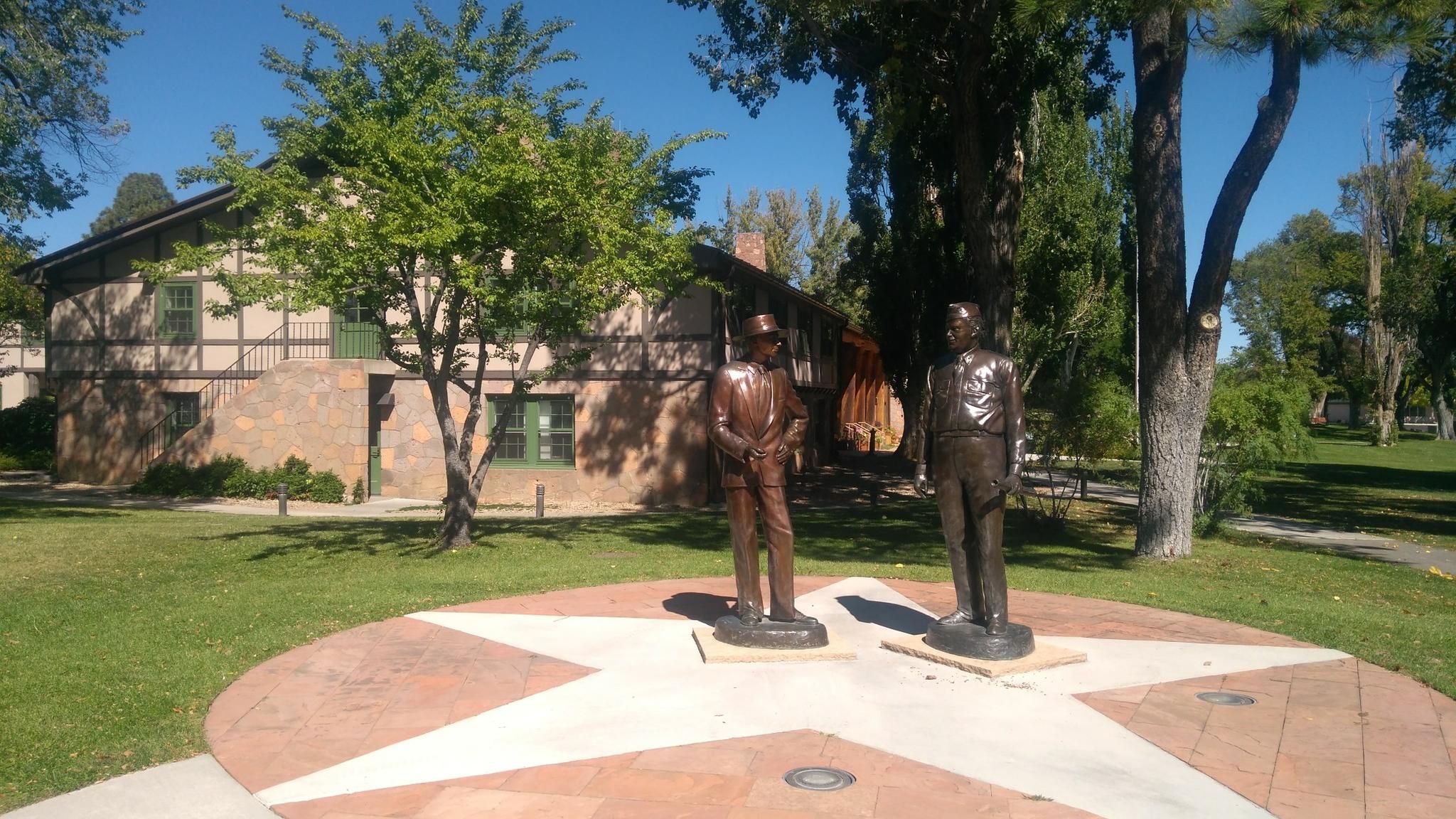 Two bronze statues stand on a star-shaped base in a sunny park. - Canyon Rim Loop