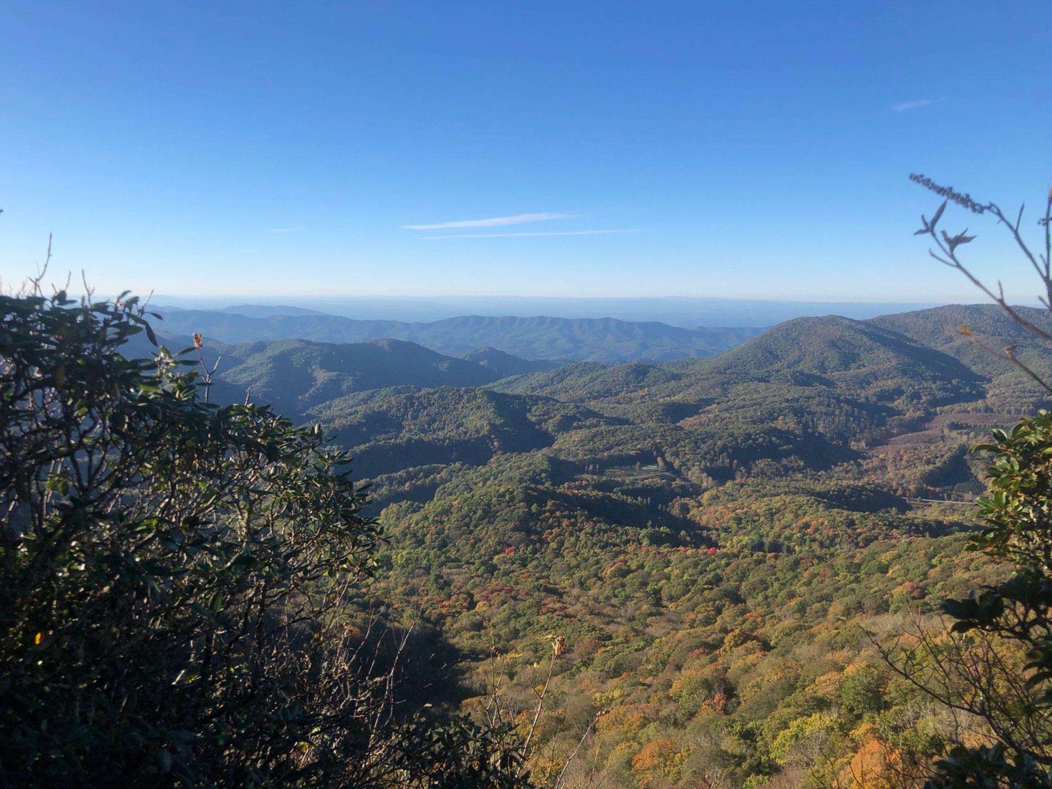 Vast mountain landscape with forested hills, autumn colors, and a clear blue sky.