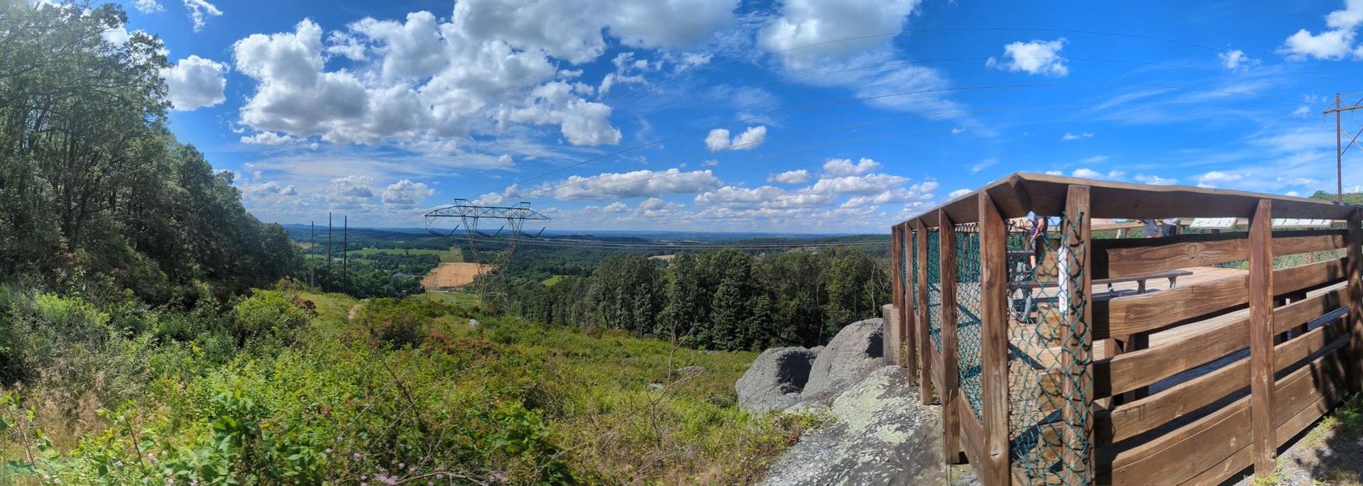 Panoramic view of a forested valley with power lines and a wooden structure.
