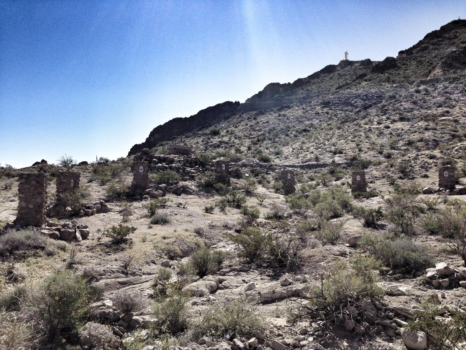 Stone pillars line a dry, rocky desert hillside under a bright sky.