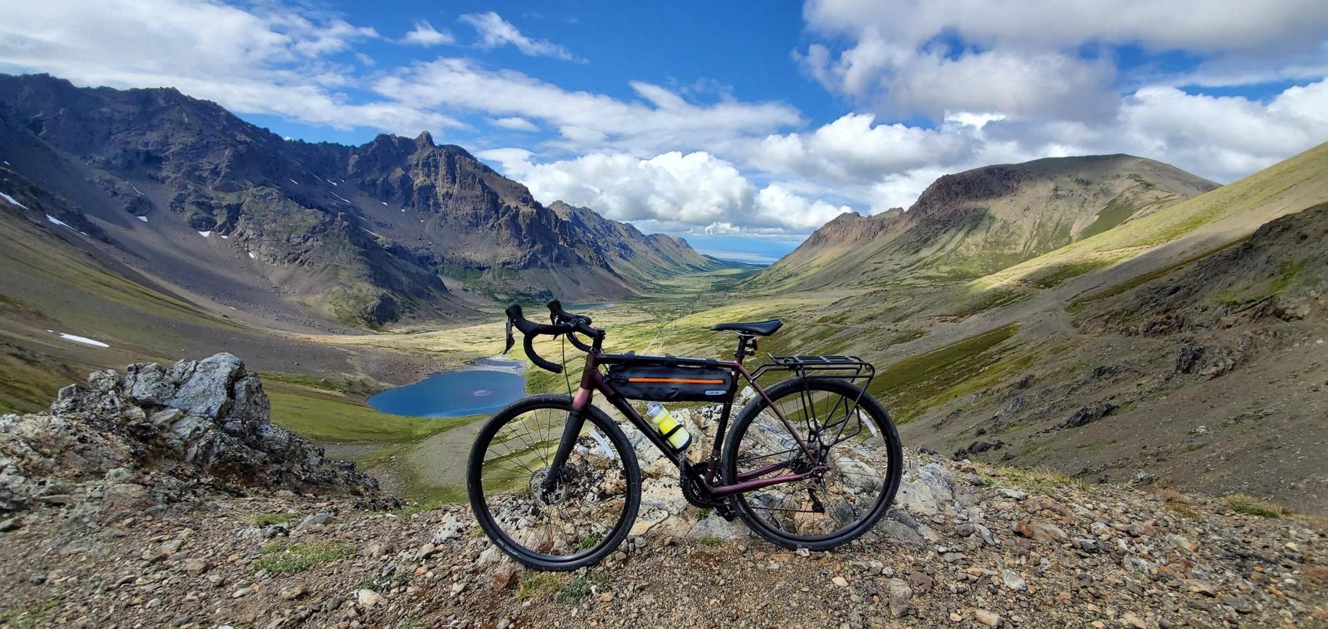 A touring bicycle overlooks a vast mountain valley with a small lake.