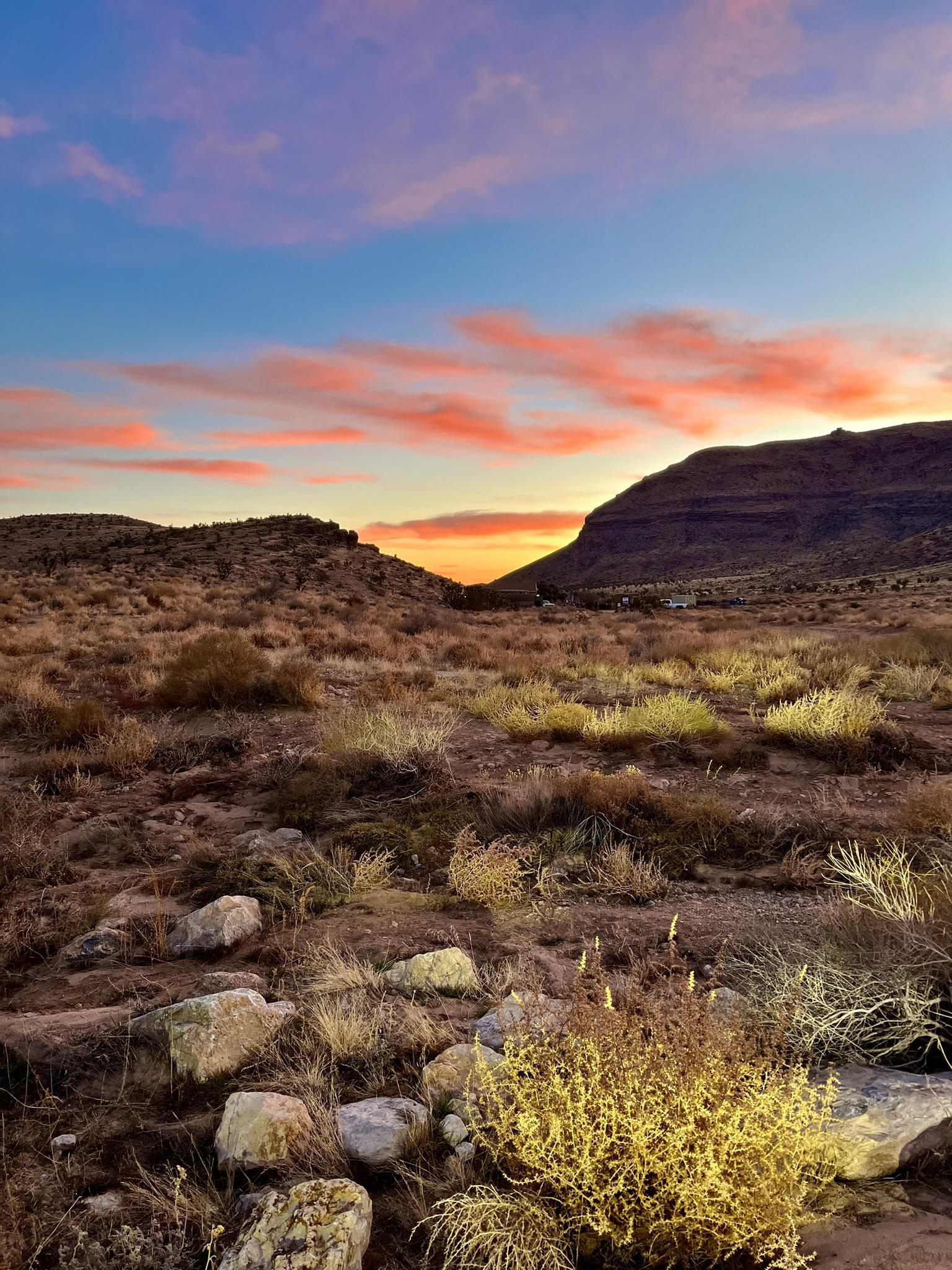Desert landscape at sunset with vibrant orange and pink clouds over mountains.