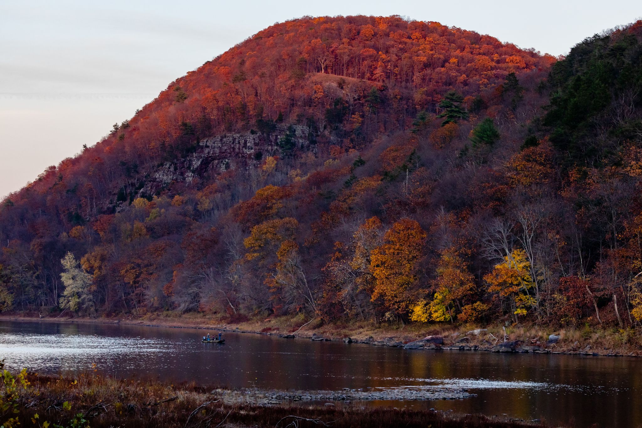 Vibrant autumn trees on a hillside beside a river with a small boat. - Susquehanna Warrior Trail