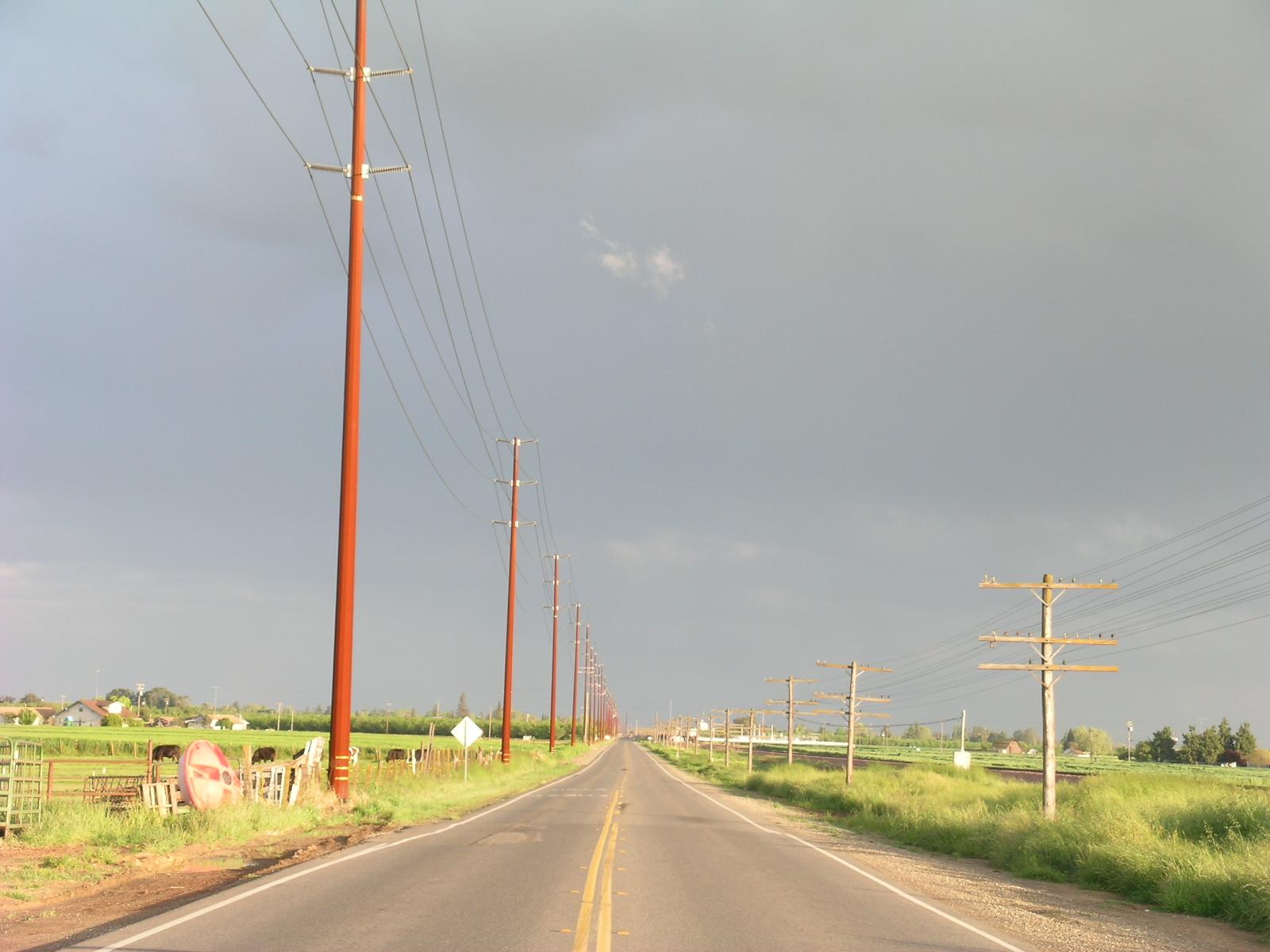 A long straight road with power lines under a cloudy, overcast sky.