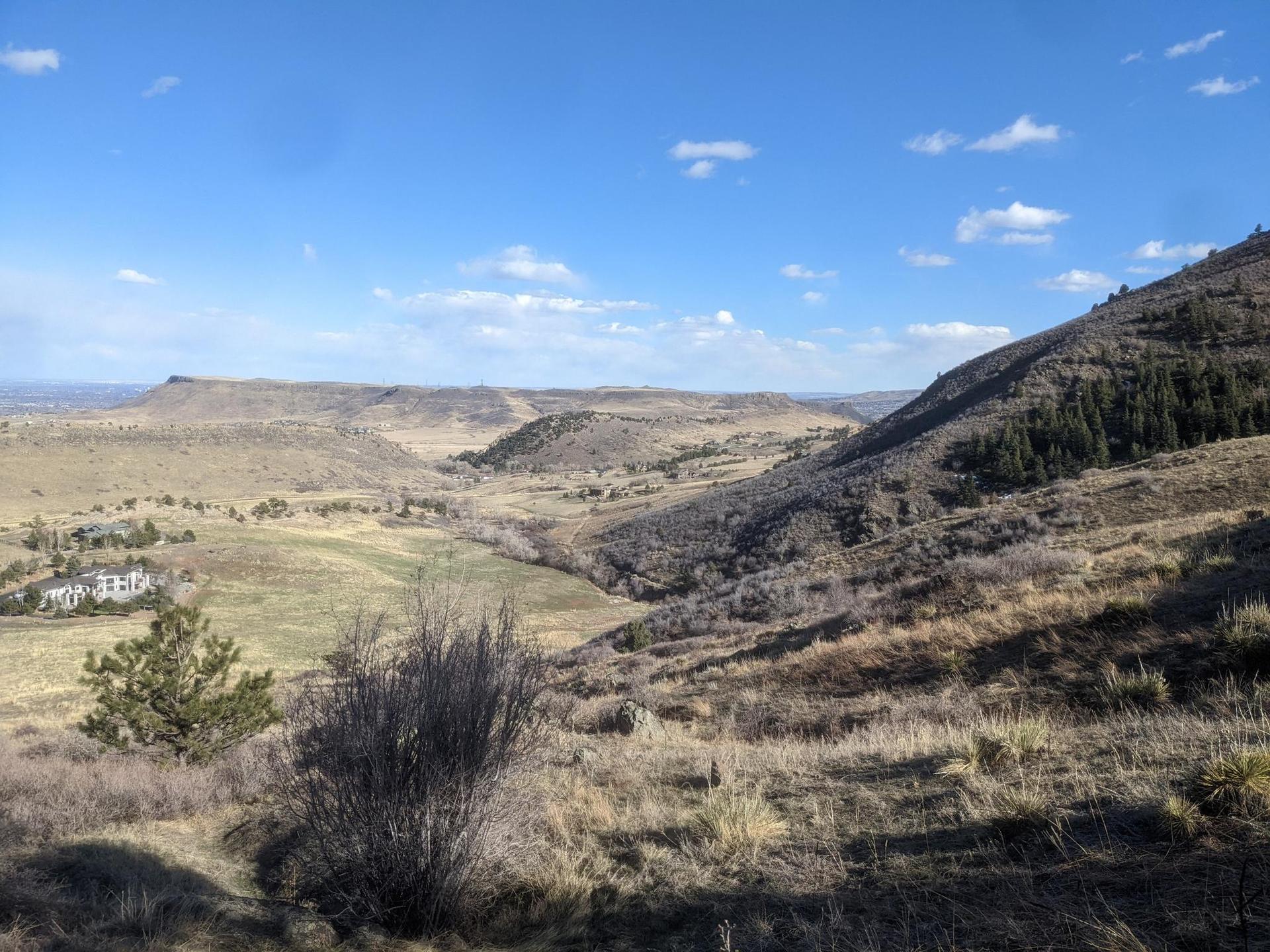 Sunny view of a wide valley with dry hills and distant mountains.
