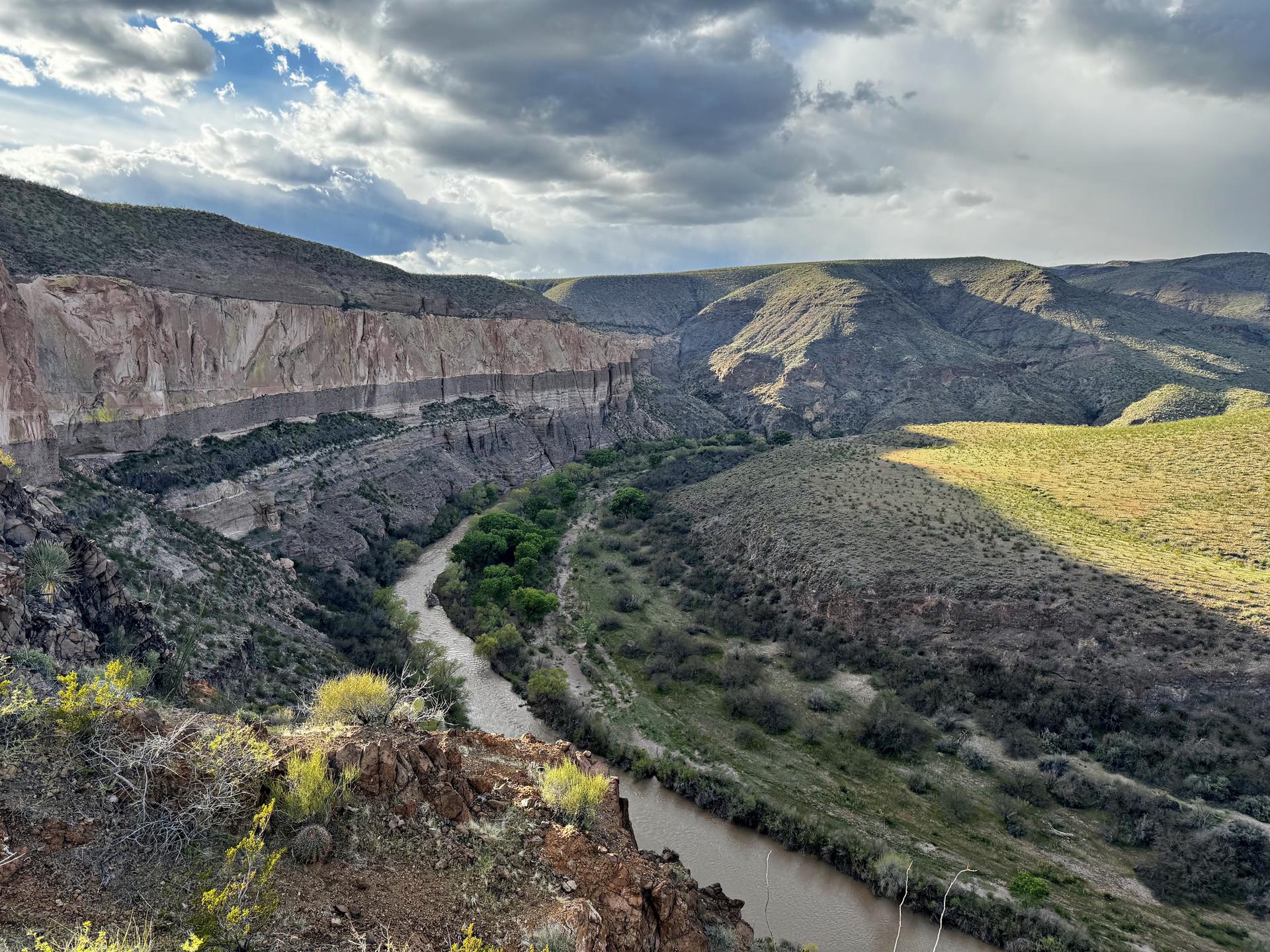 Winding river flows through a deep, rugged canyon under cloudy skies.