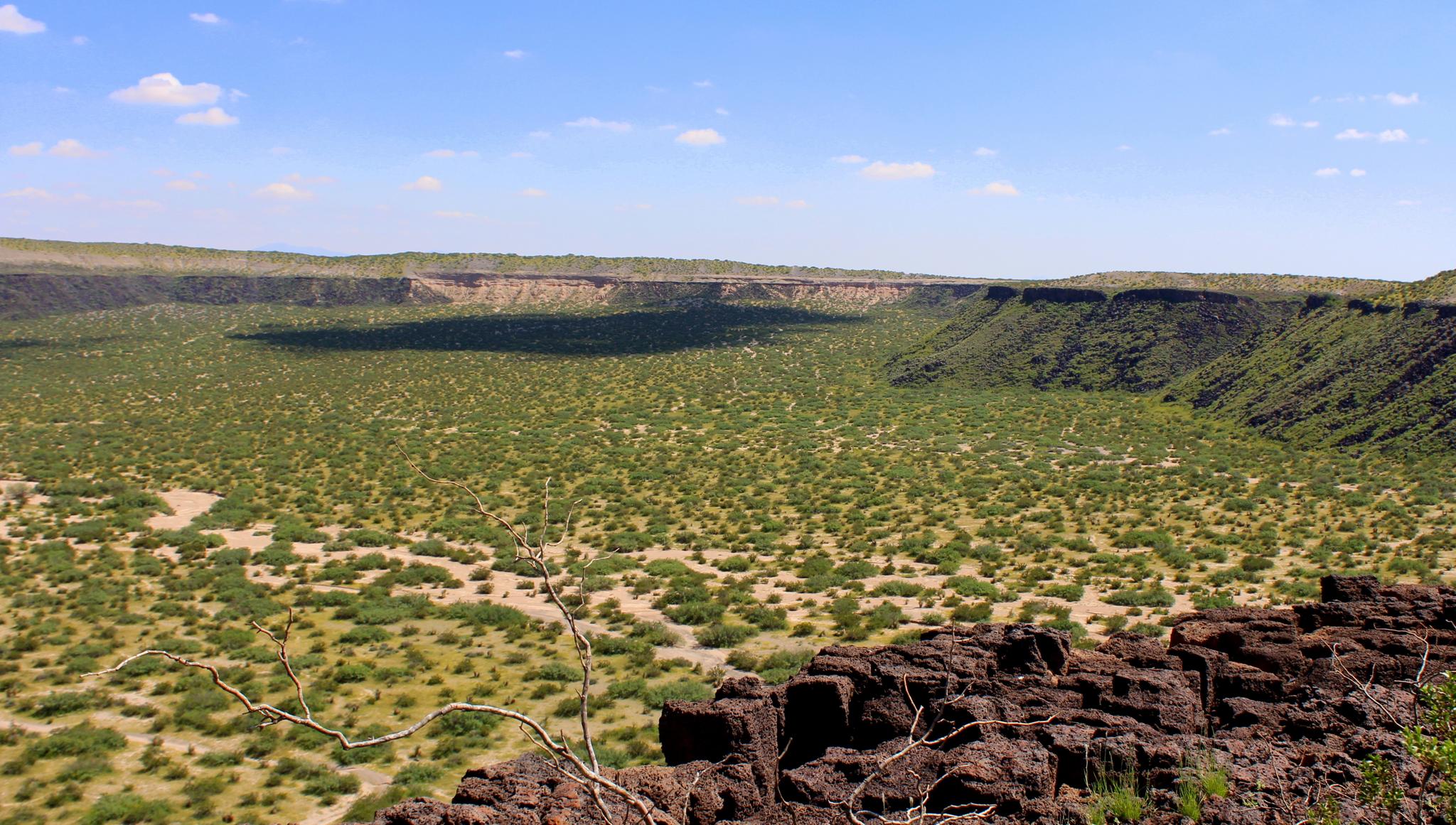 Expansive green basin with rocky walls under a bright blue sky.