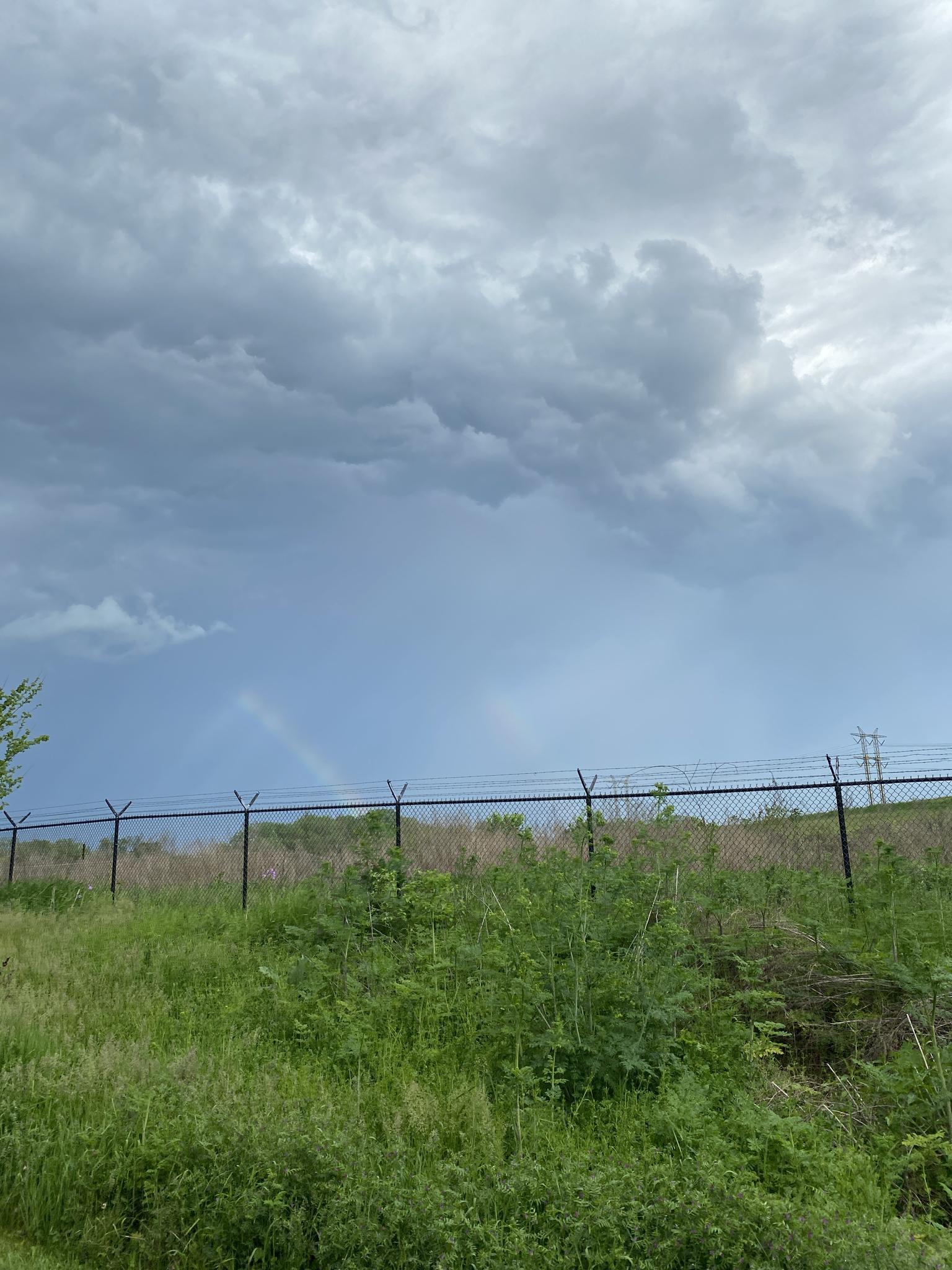 A chain-link fence tops a grassy hill under a dramatic, cloudy sky.