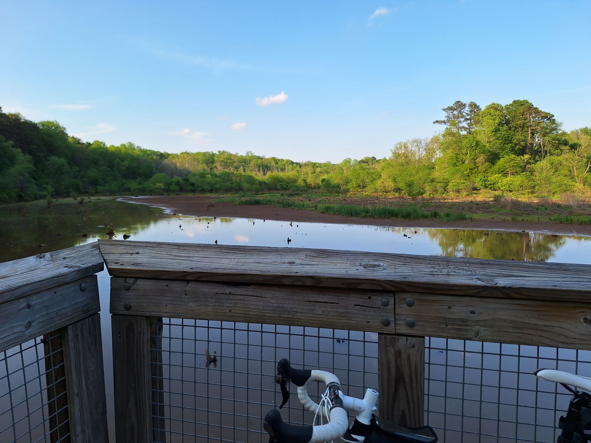 Bicycle handlebars on a wooden deck overlooking a calm lake and green forest. - Suwanee Creek Greenway