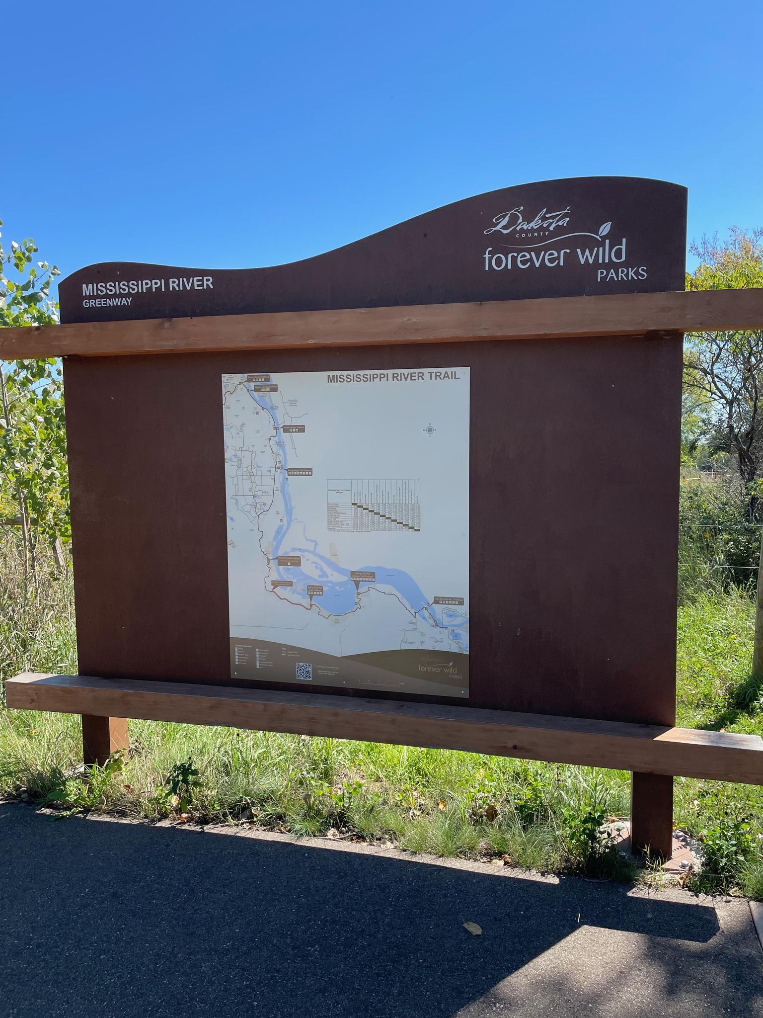 A brown information sign with a map stands under a bright blue sky.