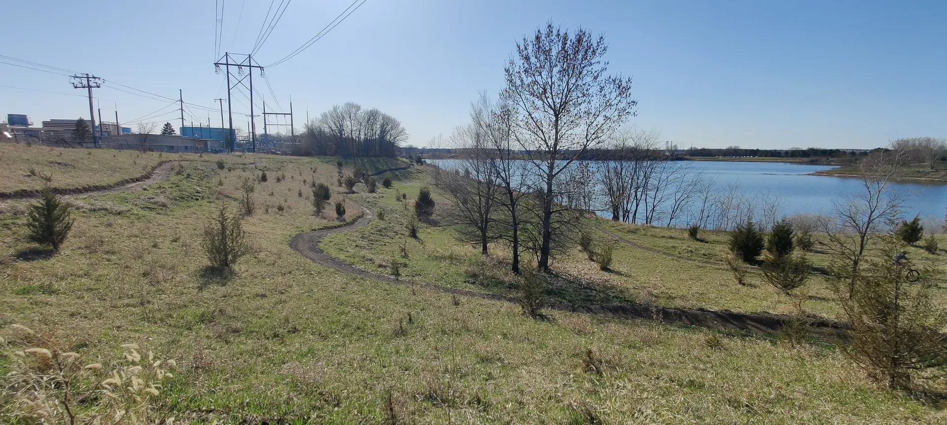 A winding path on a grassy hill overlooks a blue lake under a bright sky.