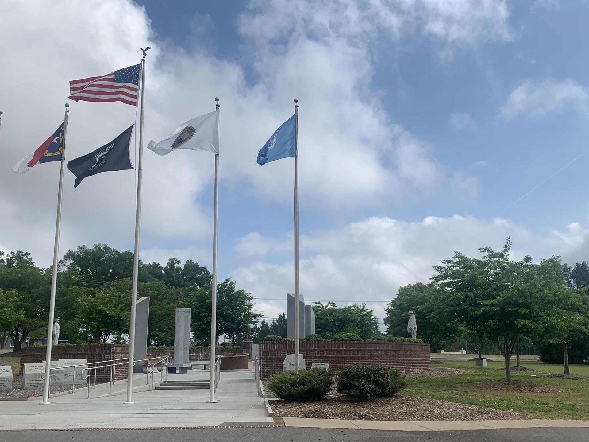 Multiple flags flying on poles near a monument under a cloudy sky.