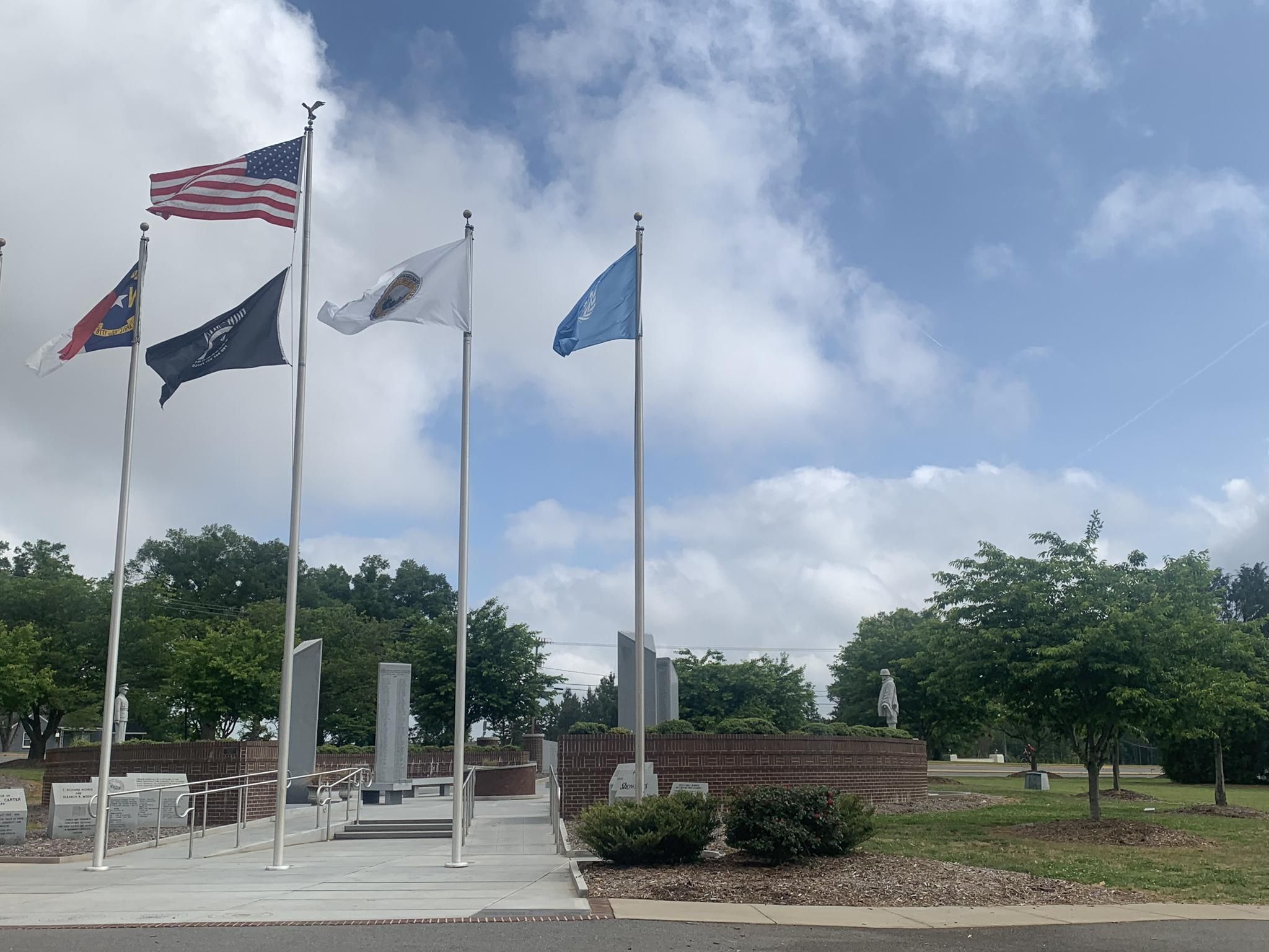 Multiple flags flying on poles near a monument under a cloudy sky. - Mint Hill loop