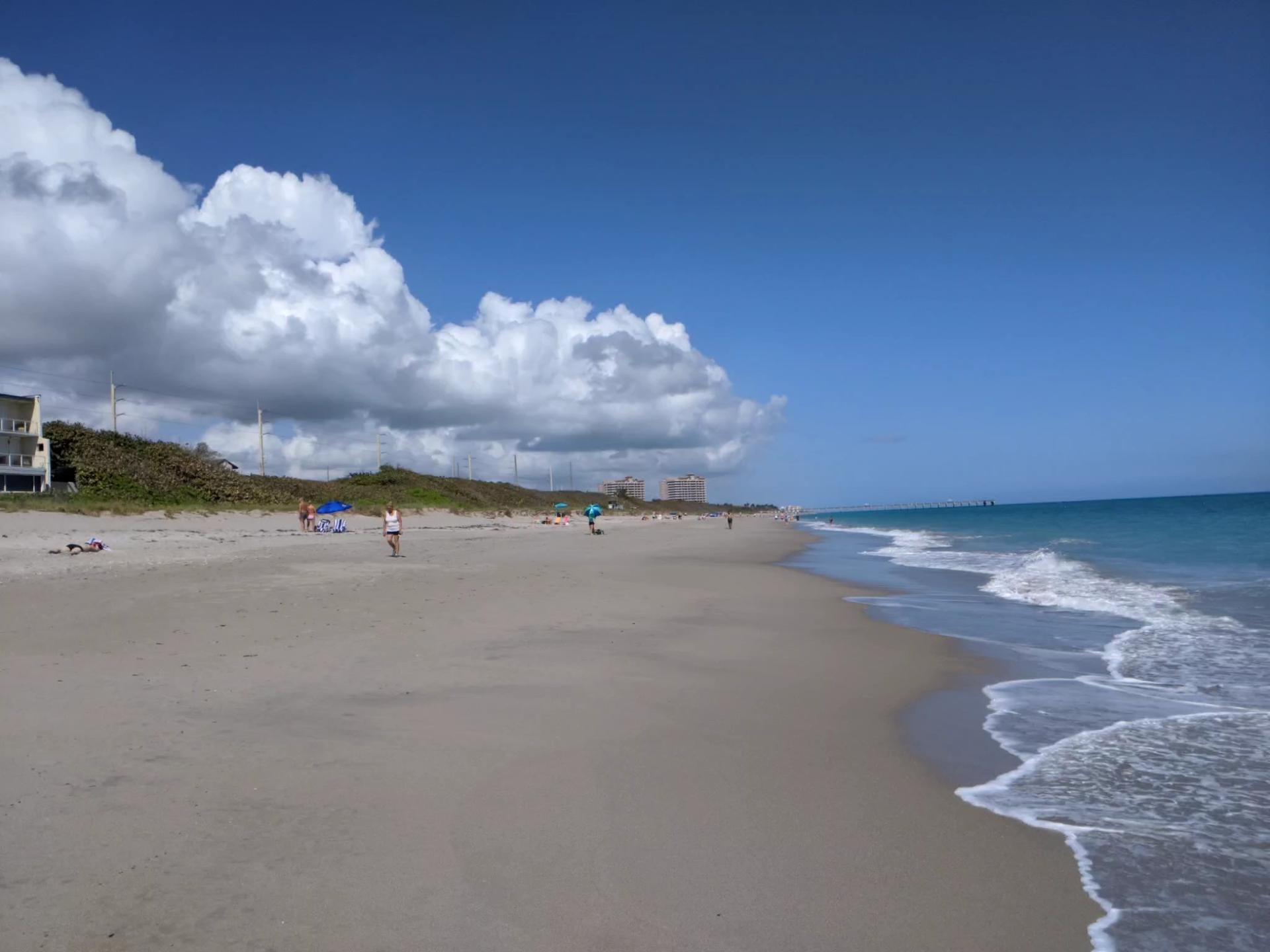 People enjoy a sunny beach with blue ocean waves and white clouds.