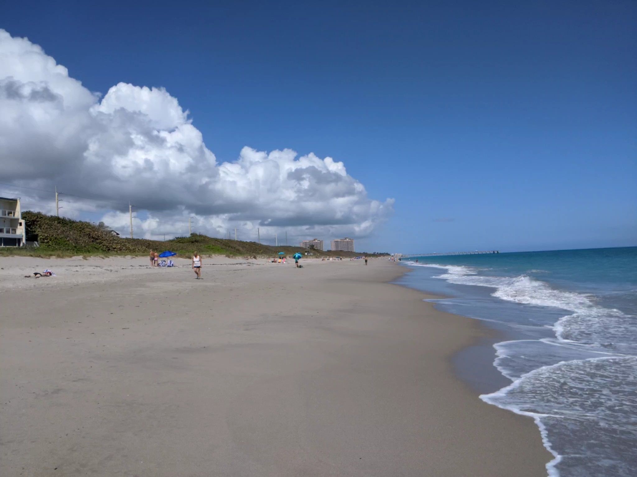 People enjoy a sunny beach with blue ocean waves and white clouds. - Jupiter loop from Roger Dean Stadium