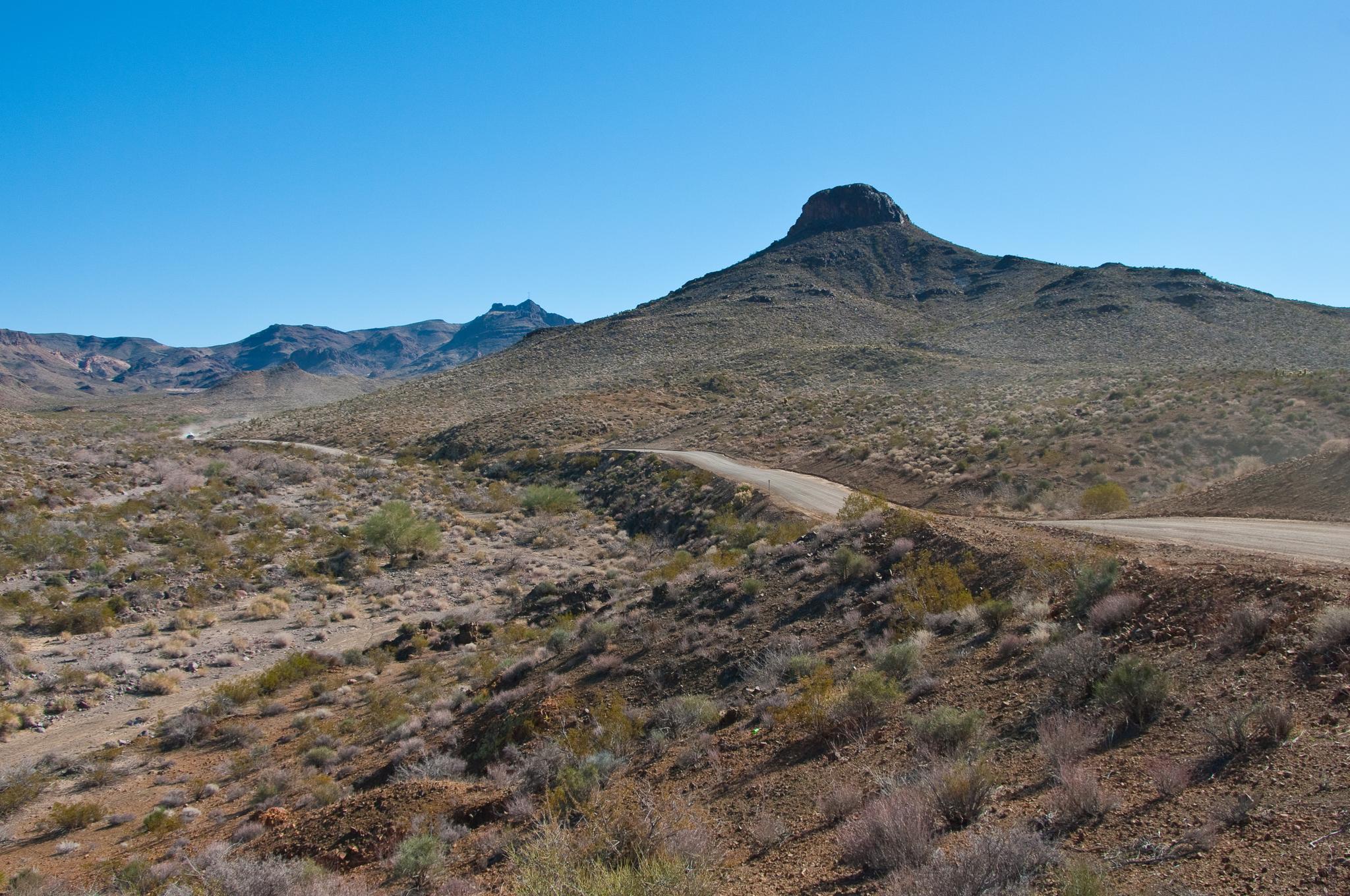 A dirt road winds through a vast arid landscape with a prominent peak.