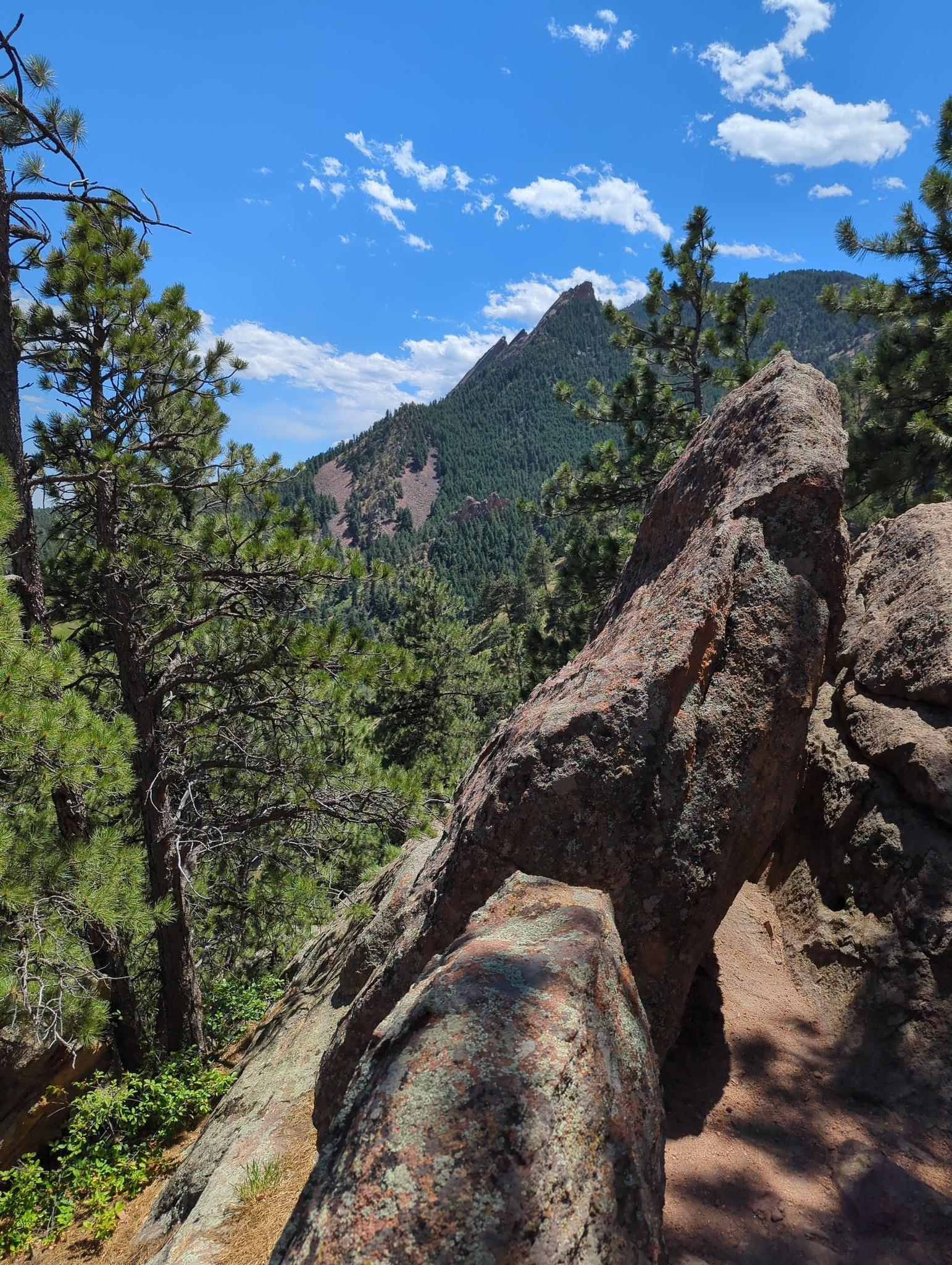 Large rocks frame a distant mountain peak under a bright blue sky.