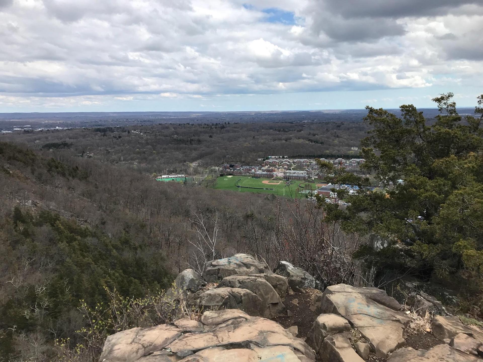Overlook of a town with a sports field, surrounded by bare trees under cloudy skies.