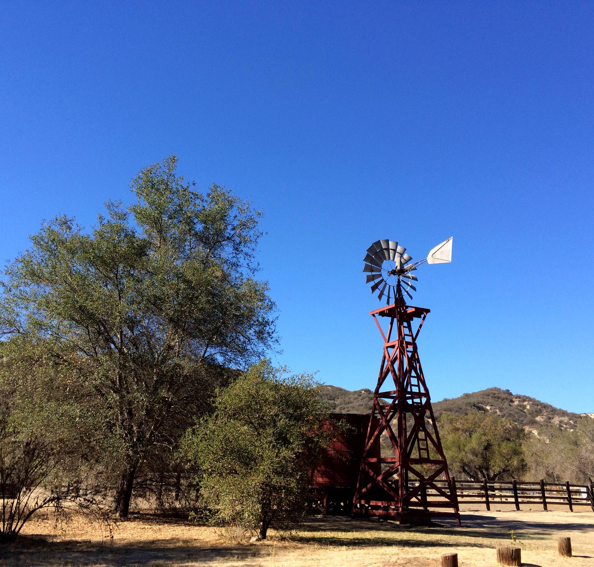 A red windmill with a white flag stands beside trees under a clear sky.
