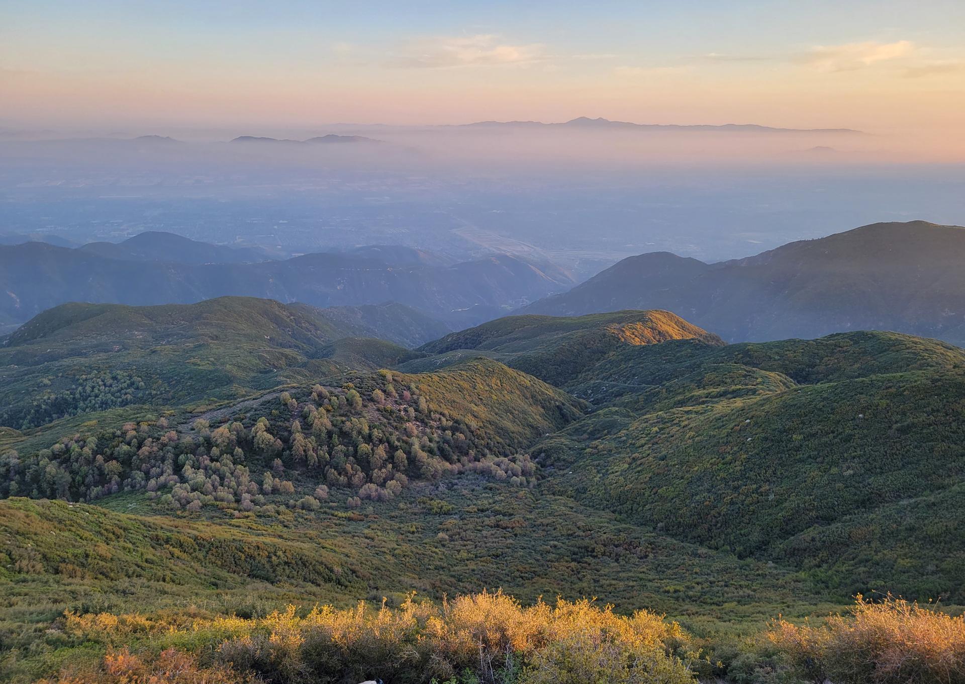 Rolling green mountains and hazy peaks bathed in warm, soft sunset light.