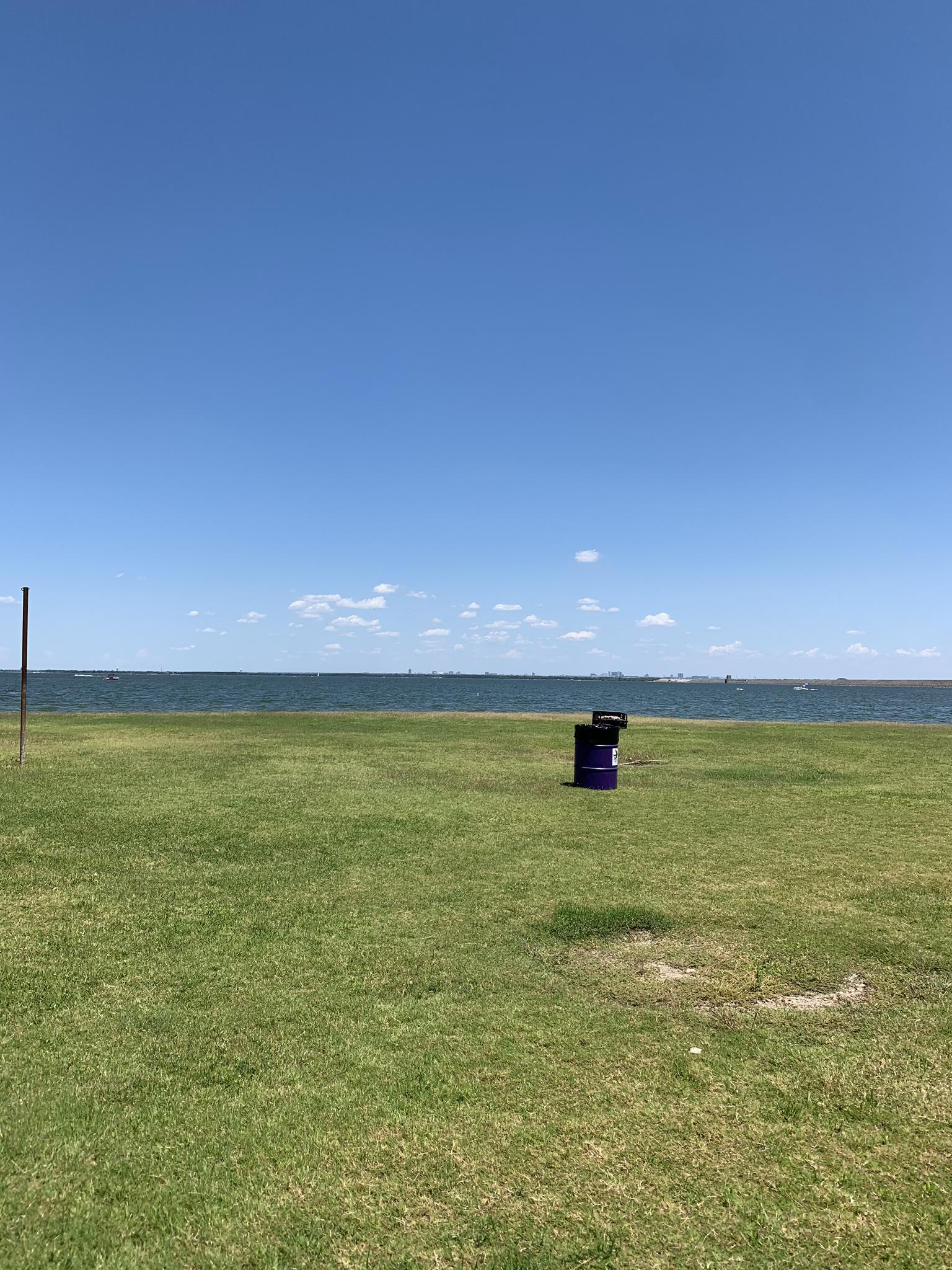 Expansive green field by a large body of water under clear blue skies.