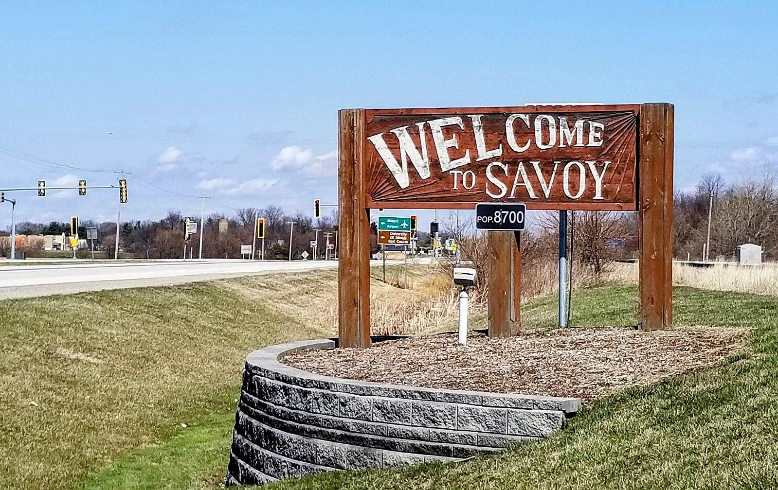 Wooden welcome sign on a grassy embankment next to a highway.