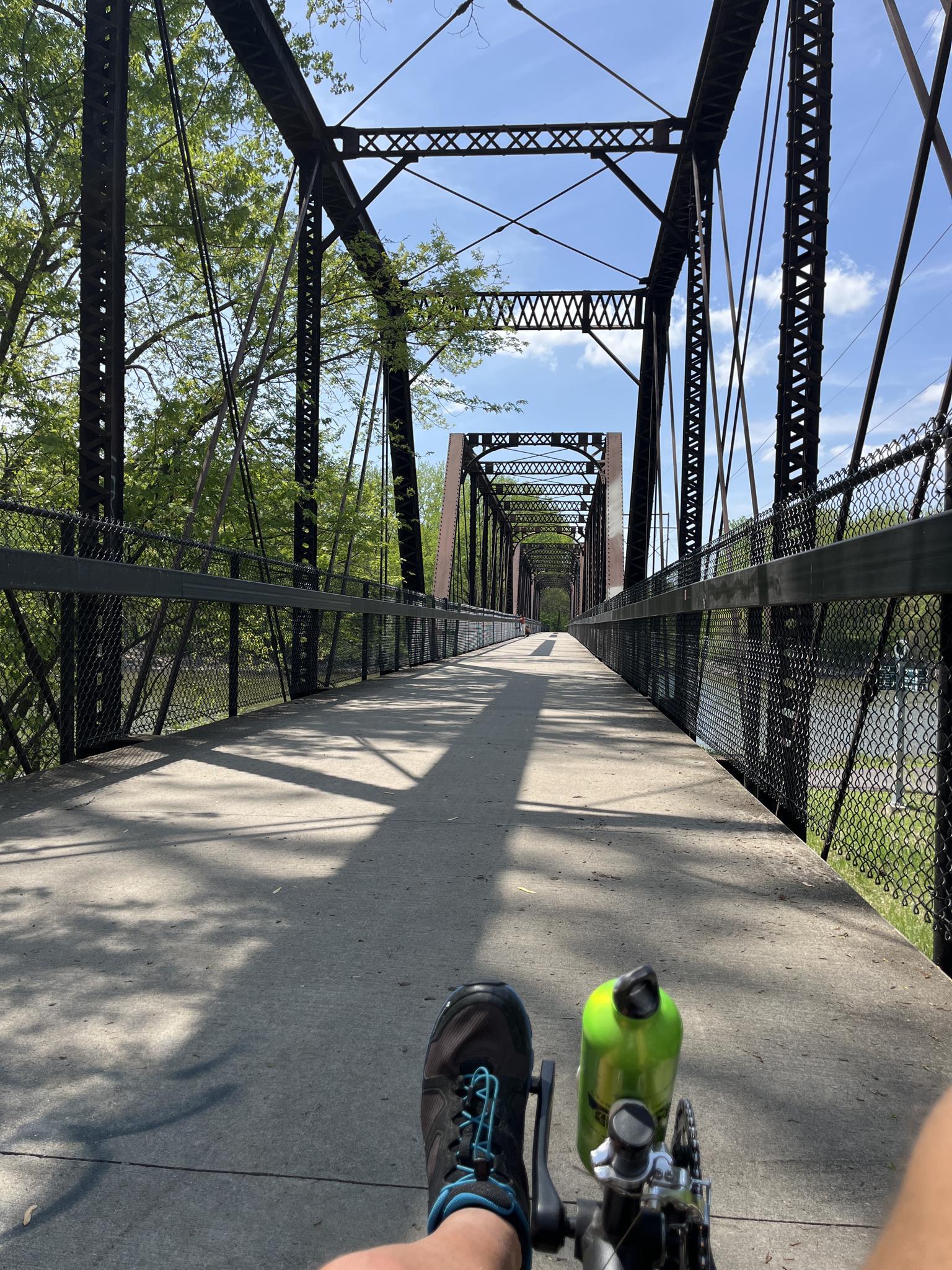 Cycling on a sunny metal truss bridge with long shadows.
