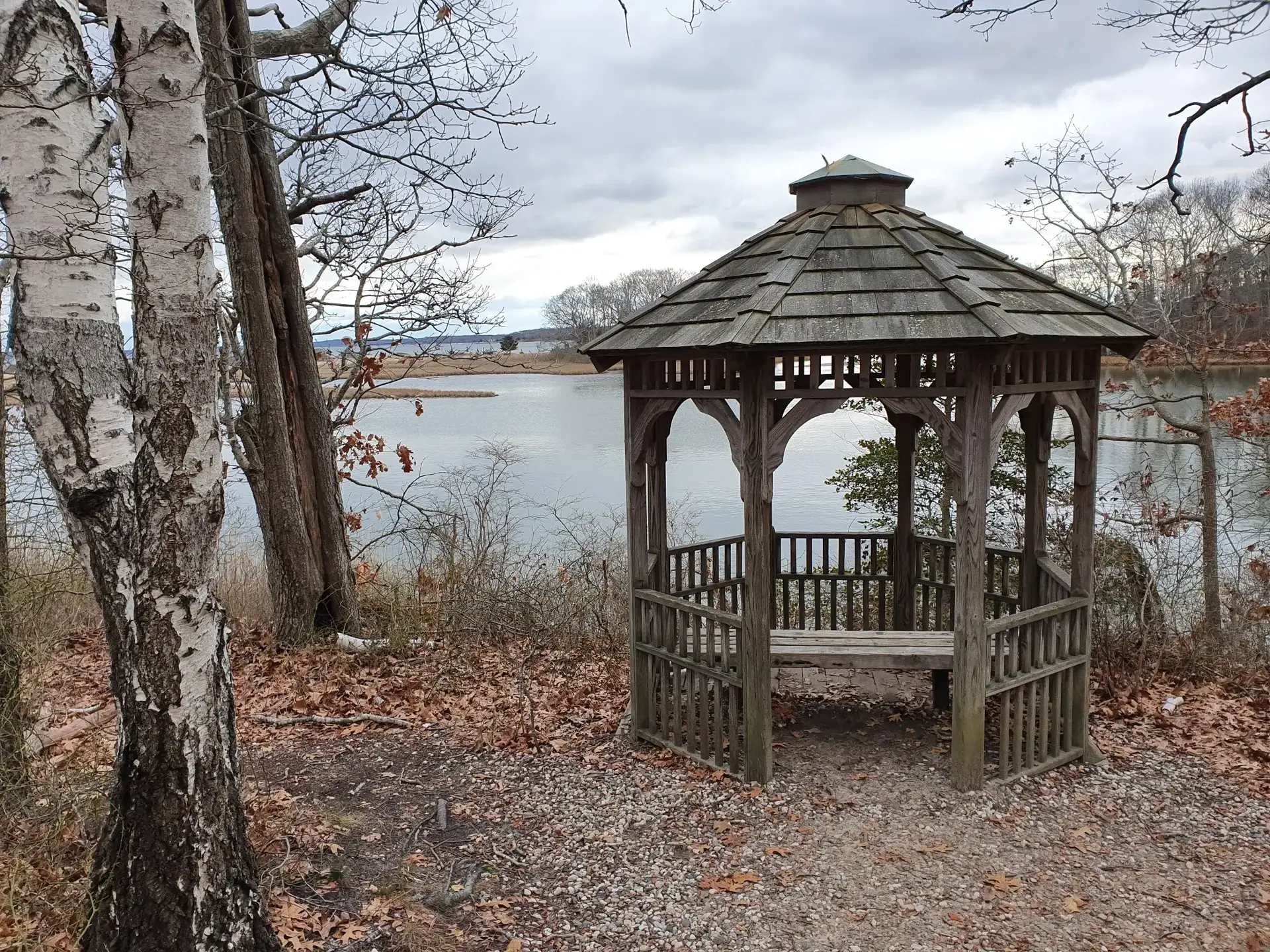 Wooden gazebo overlooking a calm body of water under an overcast sky.