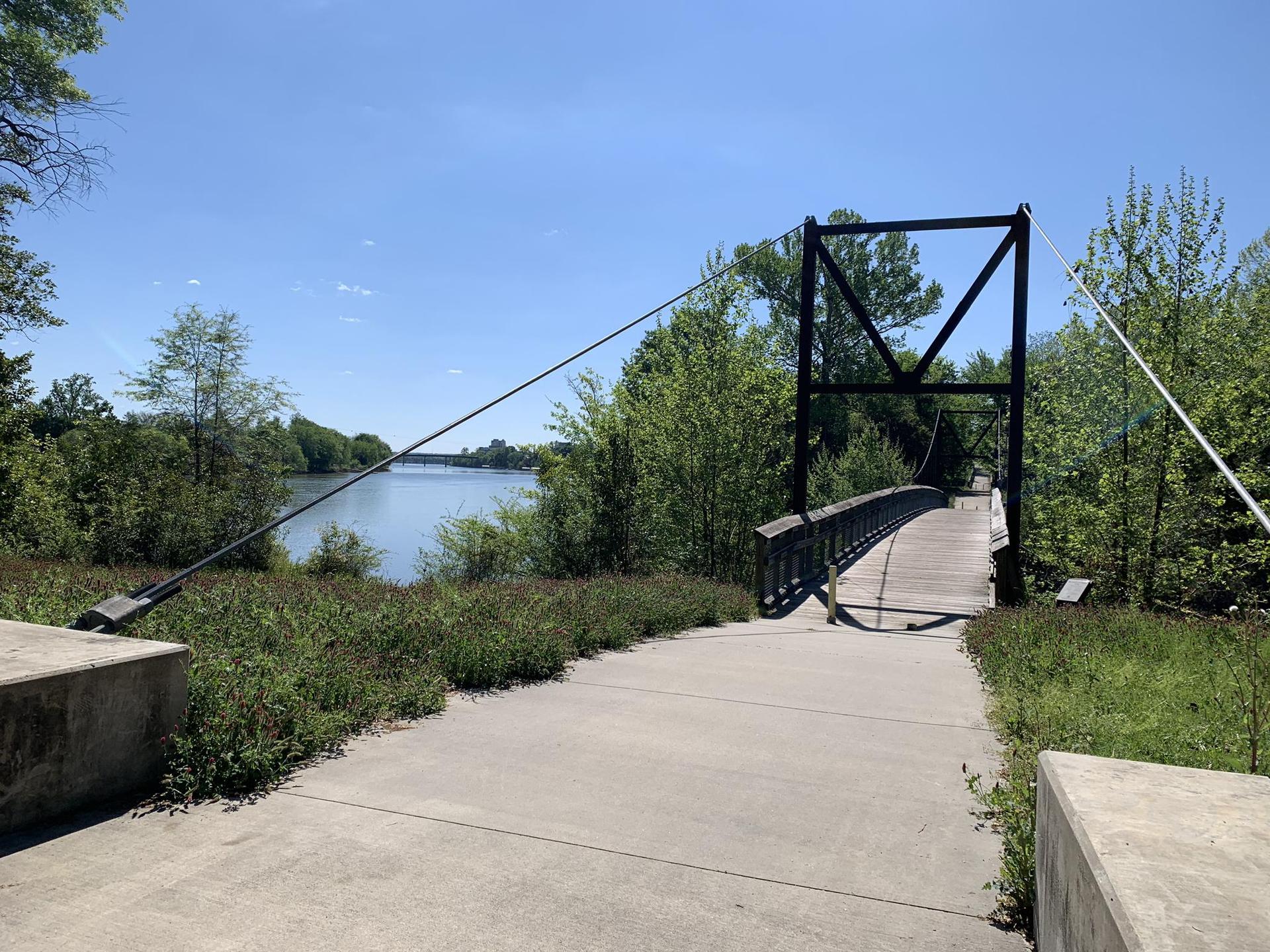 A suspension bridge extends over a wide river on a sunny day.