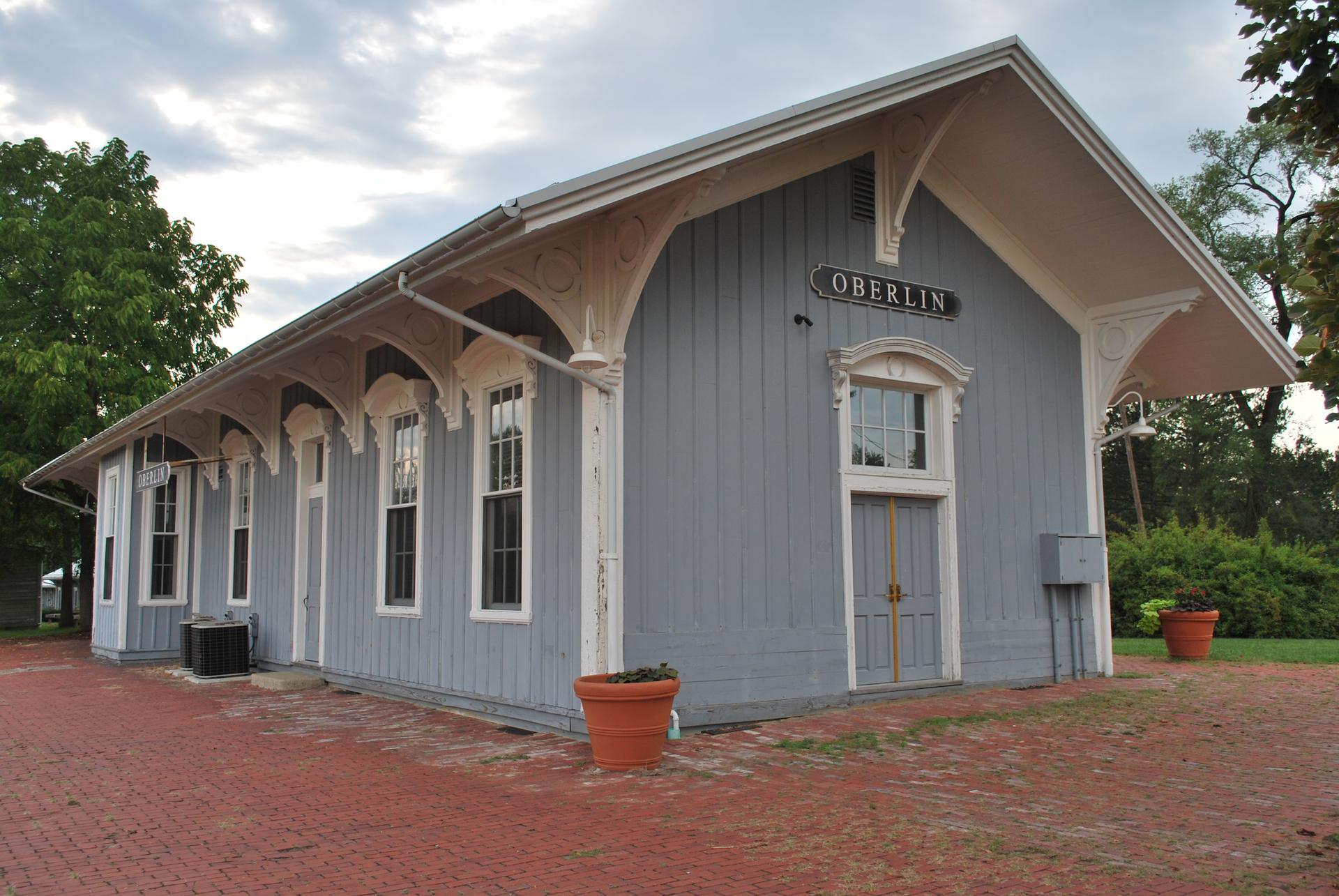 Light blue building with white trim, a sign, and red brick patio.
