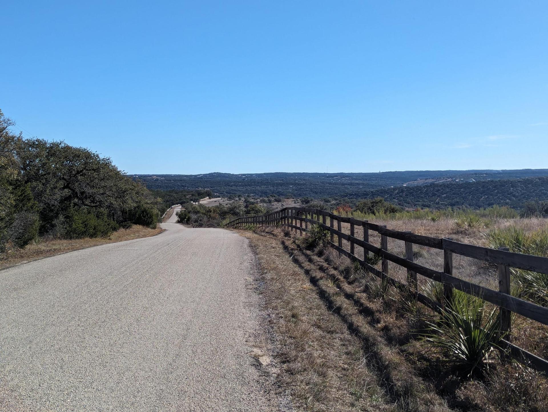Winding gravel road next to a wooden fence under a clear blue sky.