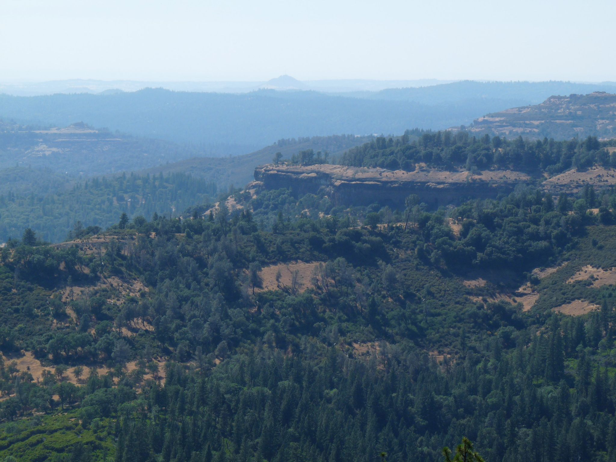 Panoramic view of a vast, hazy forested valley with distant hills and rocky cliffs. - Sunset Loop Trail