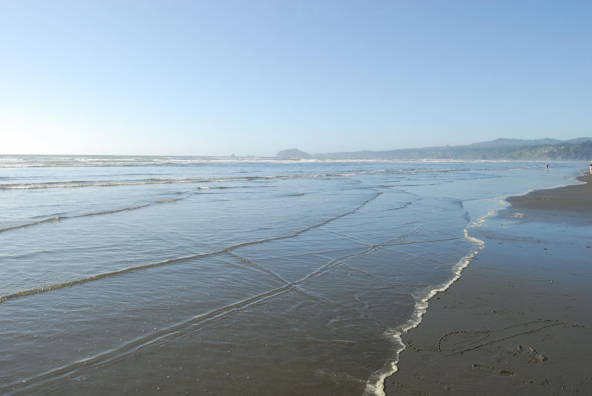 Wide sandy beach with ocean waves under a clear blue sky.