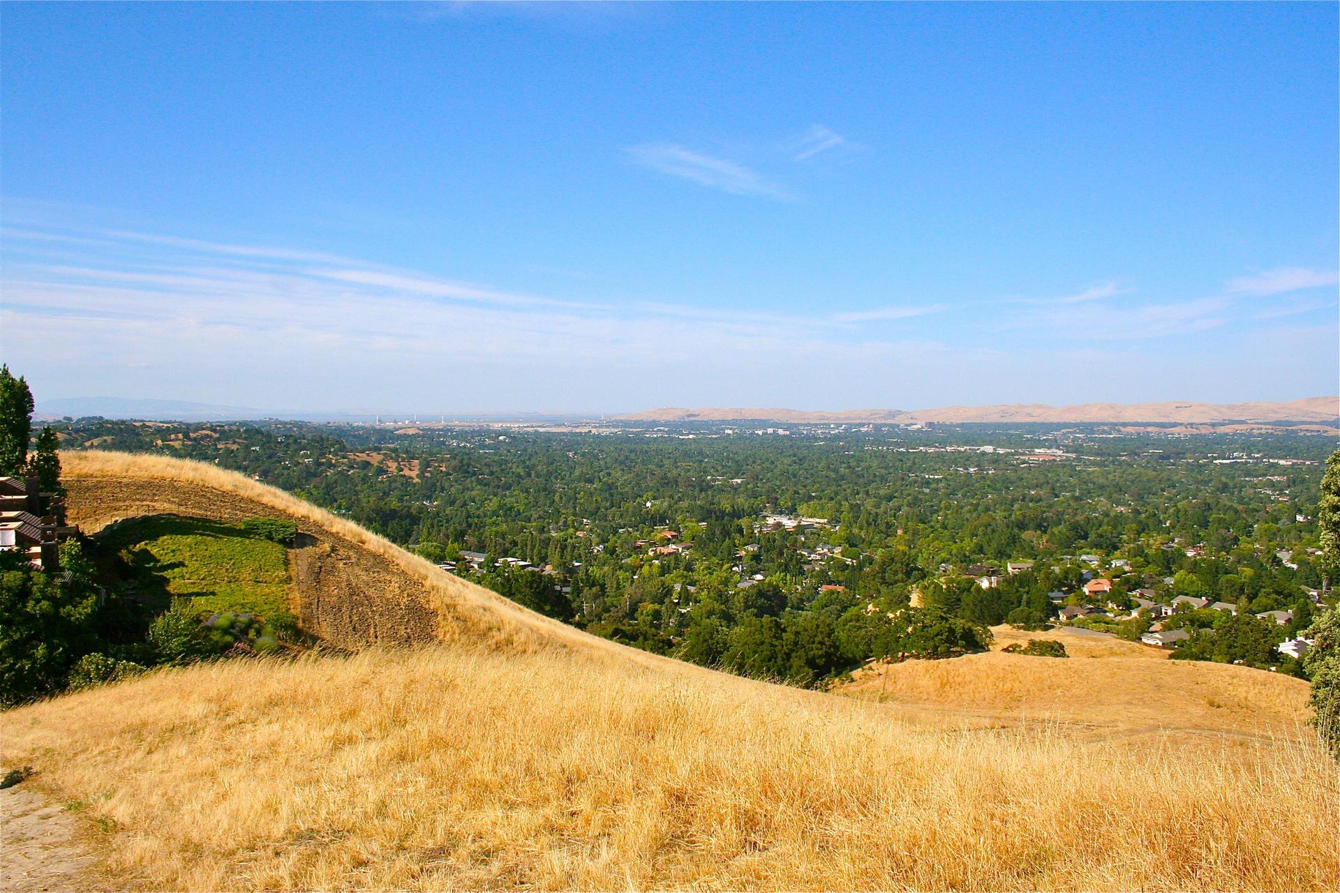 Panoramic view from a golden grassy hill overlooking a green valley under a clear sky.