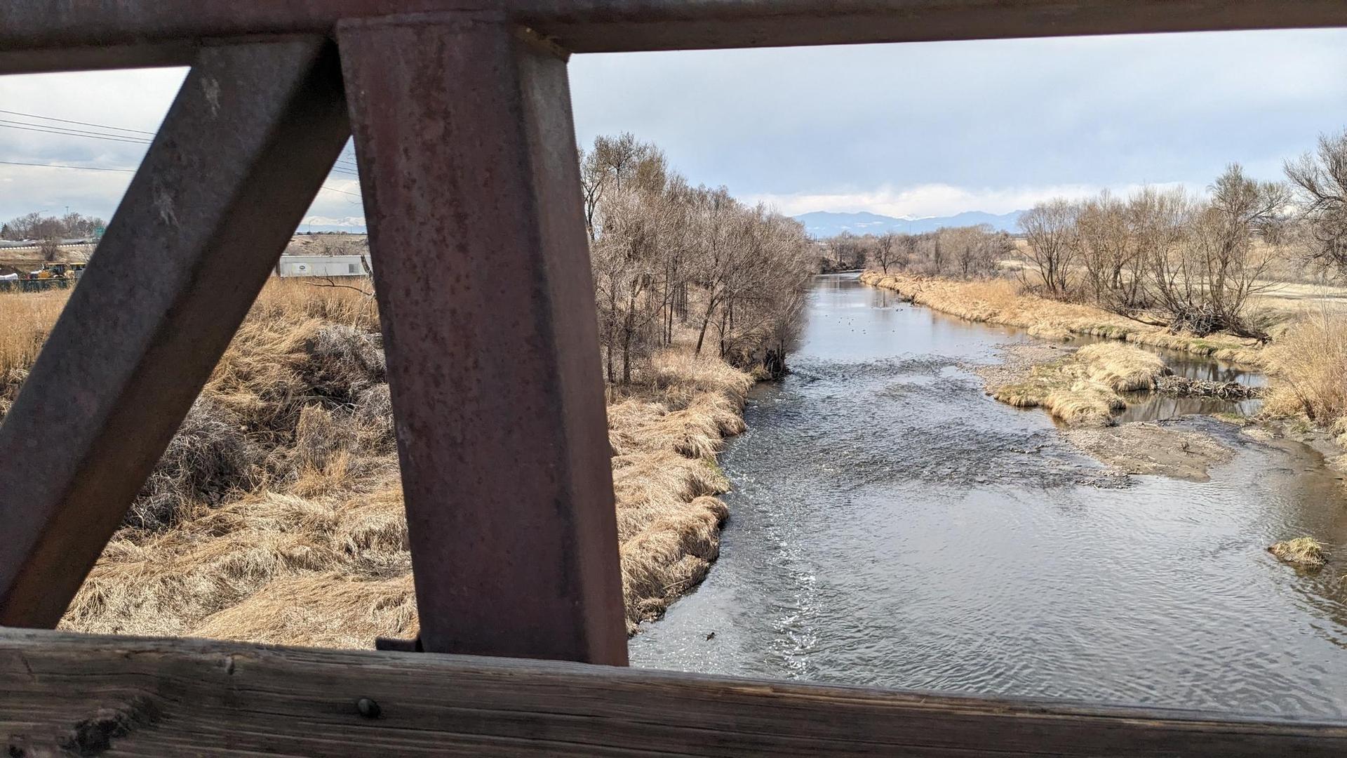 View from a bridge of a flowing river, dry banks, and distant mountains.