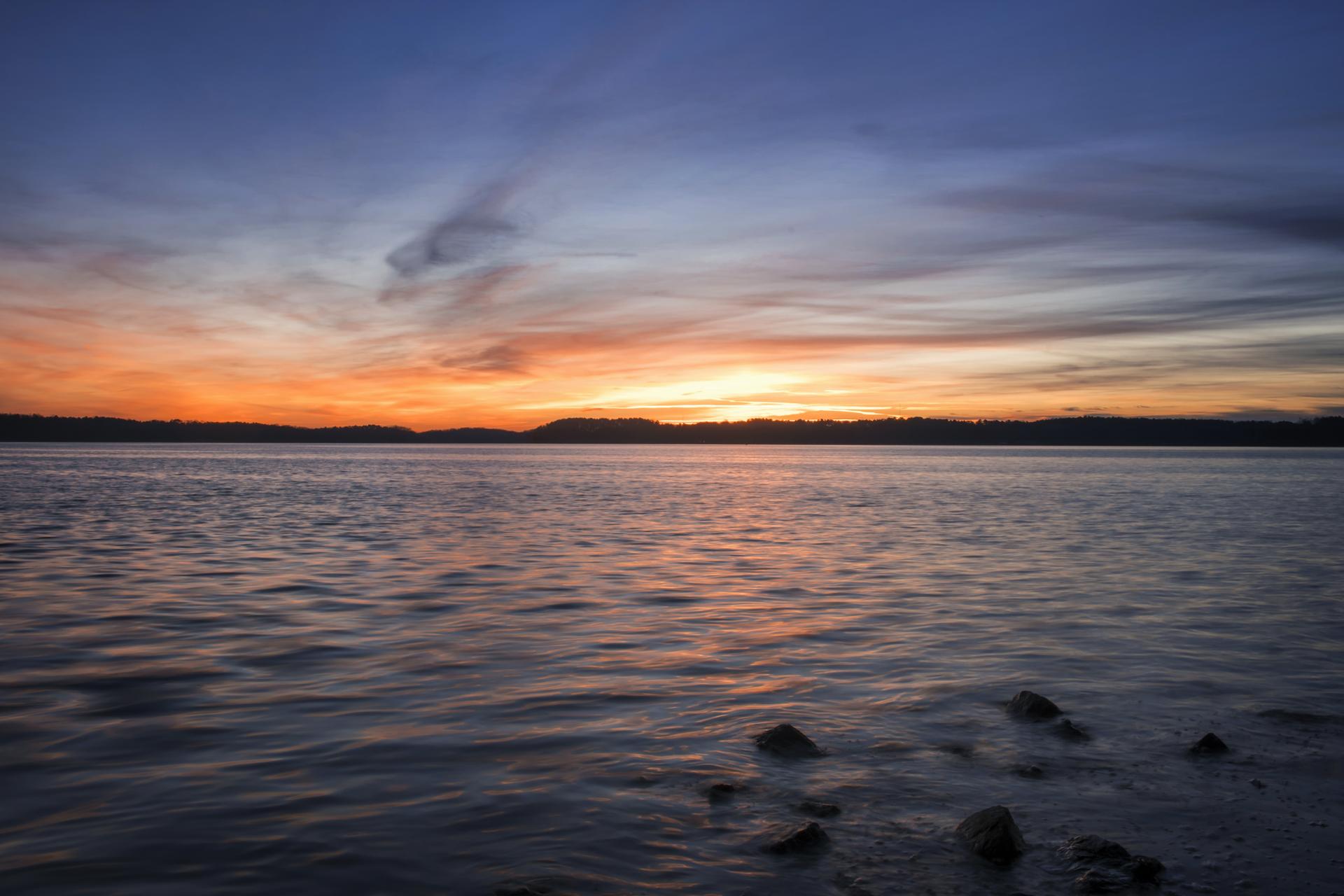 Vast water reflecting a vibrant sunset sky with orange and blue hues.