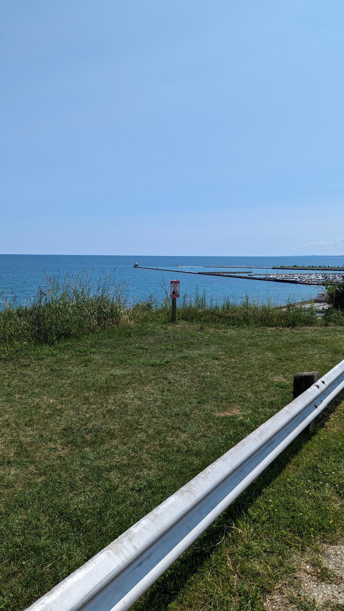 Calm blue water and sky from a grassy shore on a clear day.