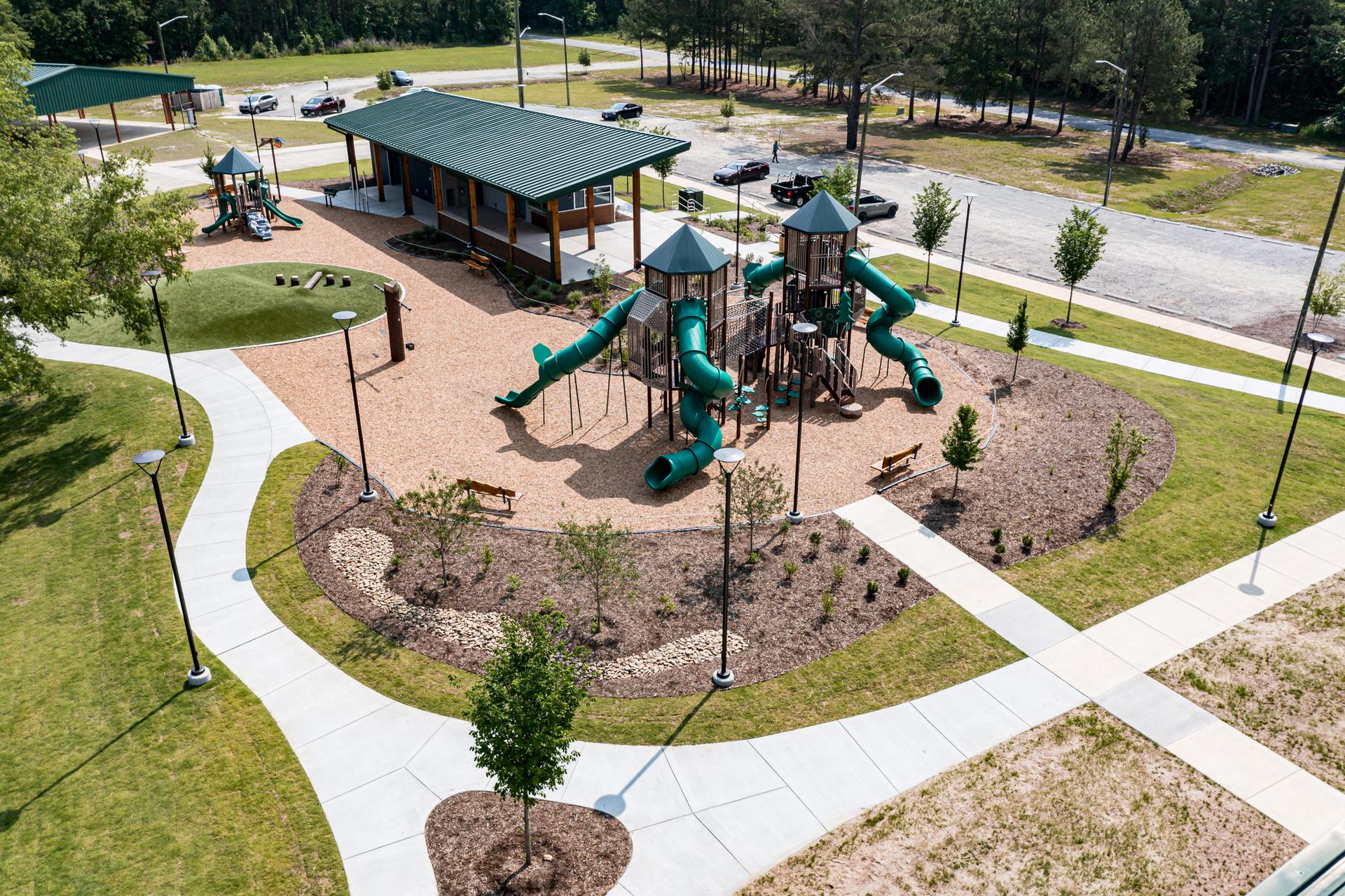 Aerial view of a bright, empty park playground with green structures and pavilion.
