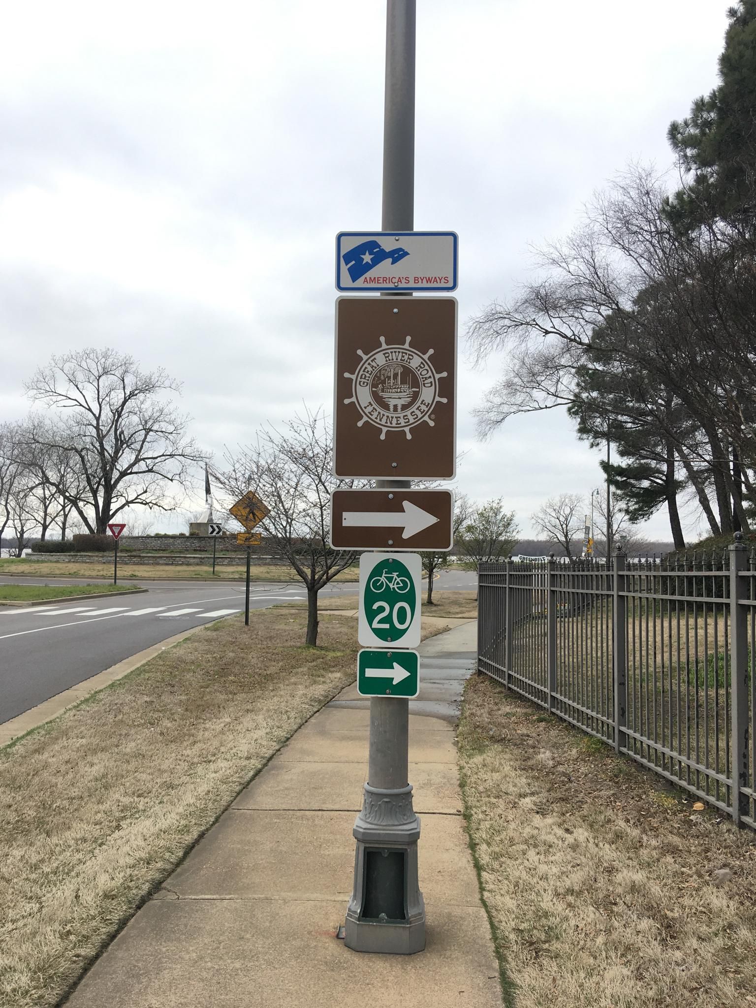 A street pole with multiple brown and green directional signs on an overcast day. - Mississippi River Trail to Meeman-Shelby Forest