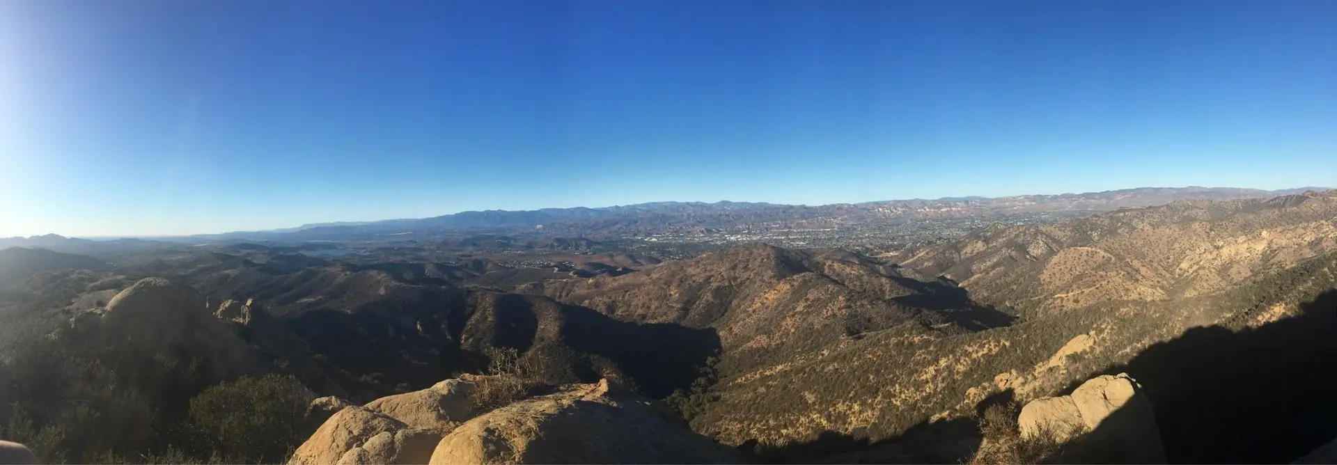 Panoramic view of rugged mountains and valleys under a clear, bright sky.