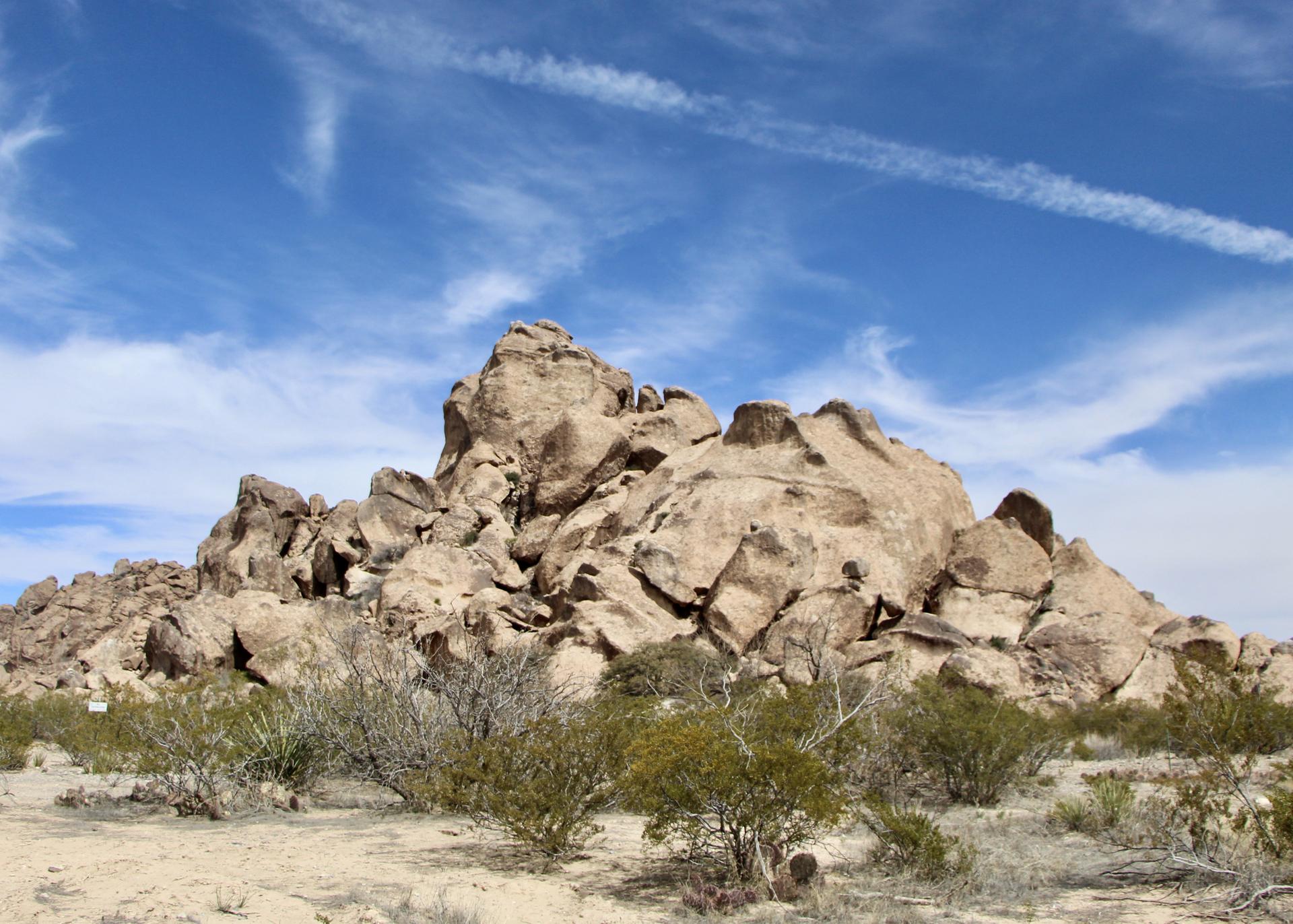Massive rock formation in a desert landscape under a bright blue sky.
