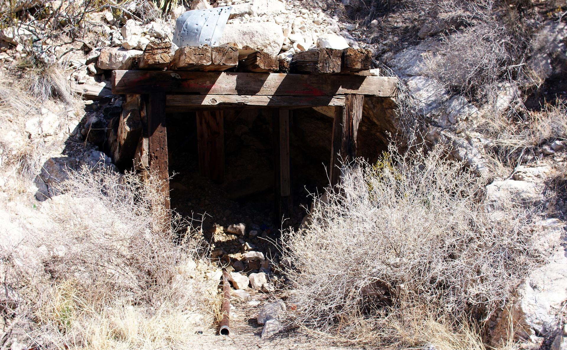 Dark, wooden mine entrance in a rocky, dry, sunlit landscape.