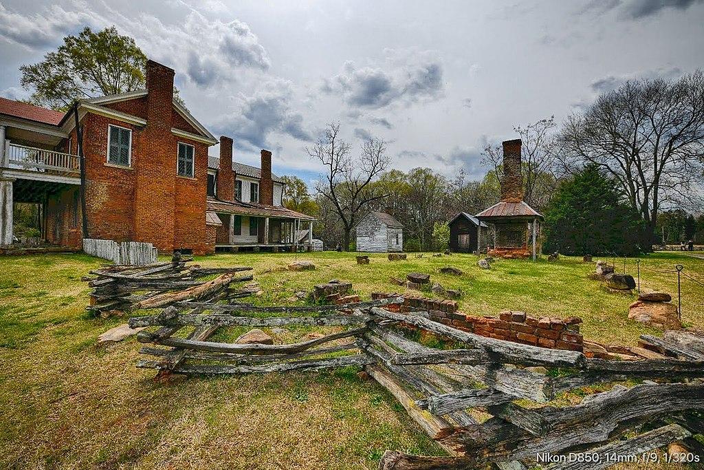 Old brick house, split rail fence, and chimney under a cloudy sky.