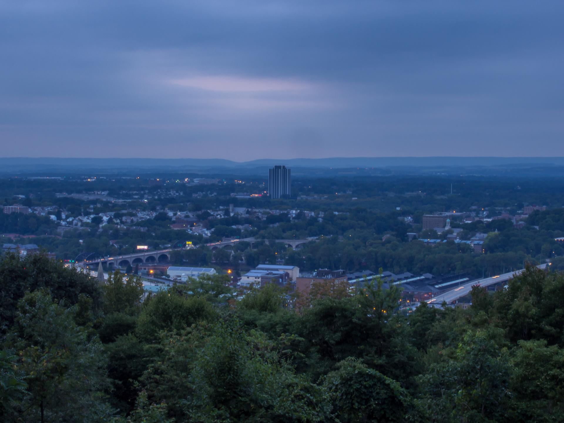 Distant city lights and buildings viewed from a high vantage point at dusk.